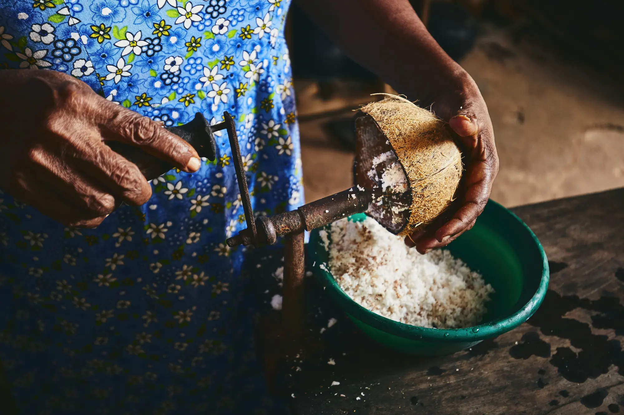 Sri Lankan woman wearing a blue dress, grating coconut into a green bowl during a cooking class in Tangalle.