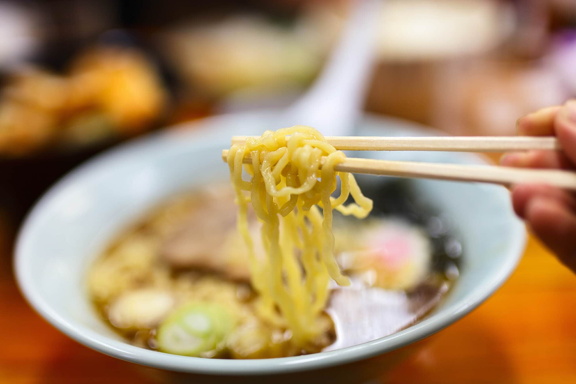 Close up of hand holding chopsticks with ramen noodles at Umibozu Ramen Bar, one of the best restaurants in Kuta Lombok.