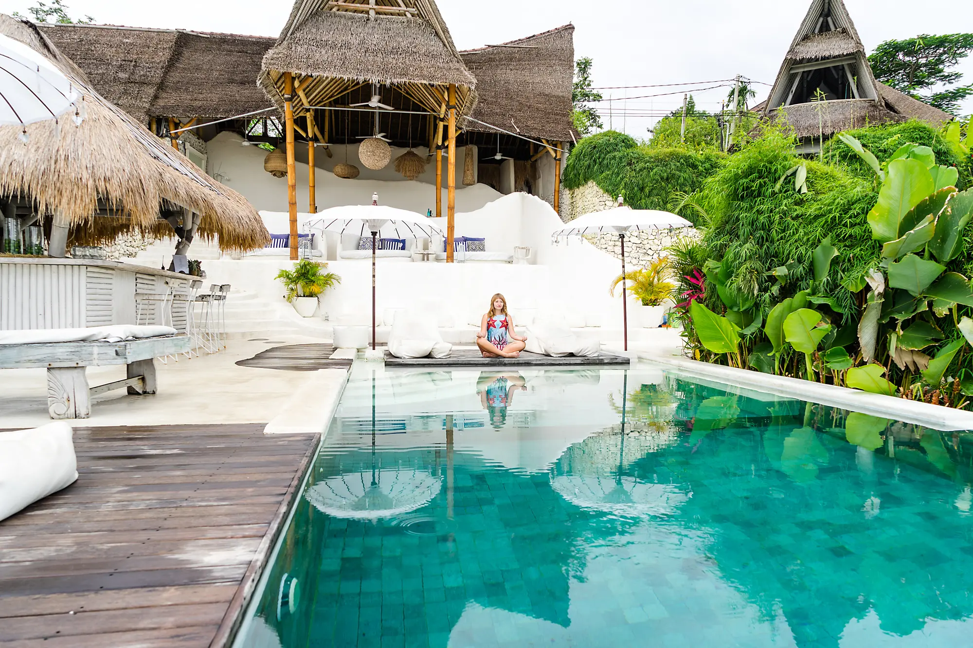 Woman sitting in front of a white wall and turquoise pool at Gravity Hotel in Uluwatu, one of the best areas to stay in Bali.