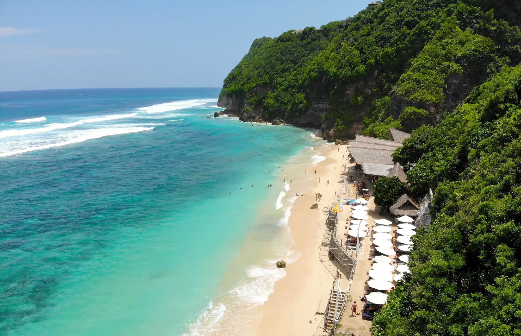 Aerial view of white sand beach, turquoise water and rows of white umbrellas at Sundays Beach Club, one of the best beaches in Uluwatu Bali.