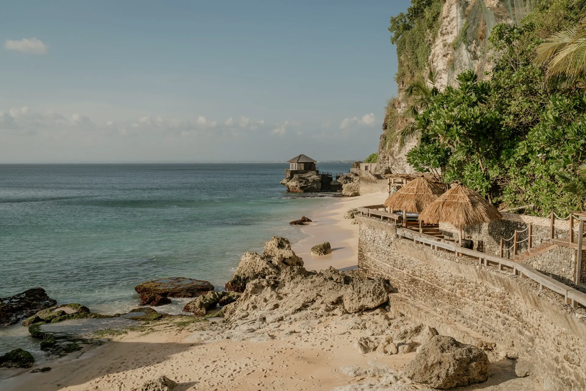 View of a private beach club set against a lush cliff on the rocky Kubu Beach, one of the best hidden gems beaches in Uluwatu Bali.