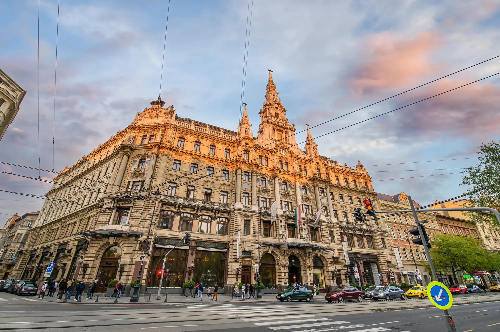 Old world beige stone building with ornate details housing New York Café during sunset on a corner in Budapest.
