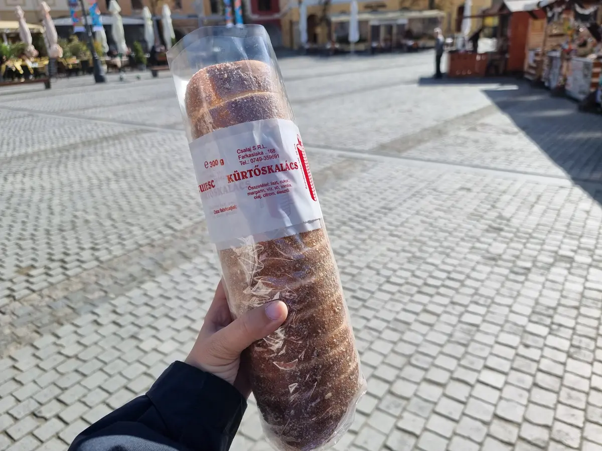 Hand holding a Hungarian Chimney Cakes (kurtos kalac) wrapped in plastic, best street food in Budapest.