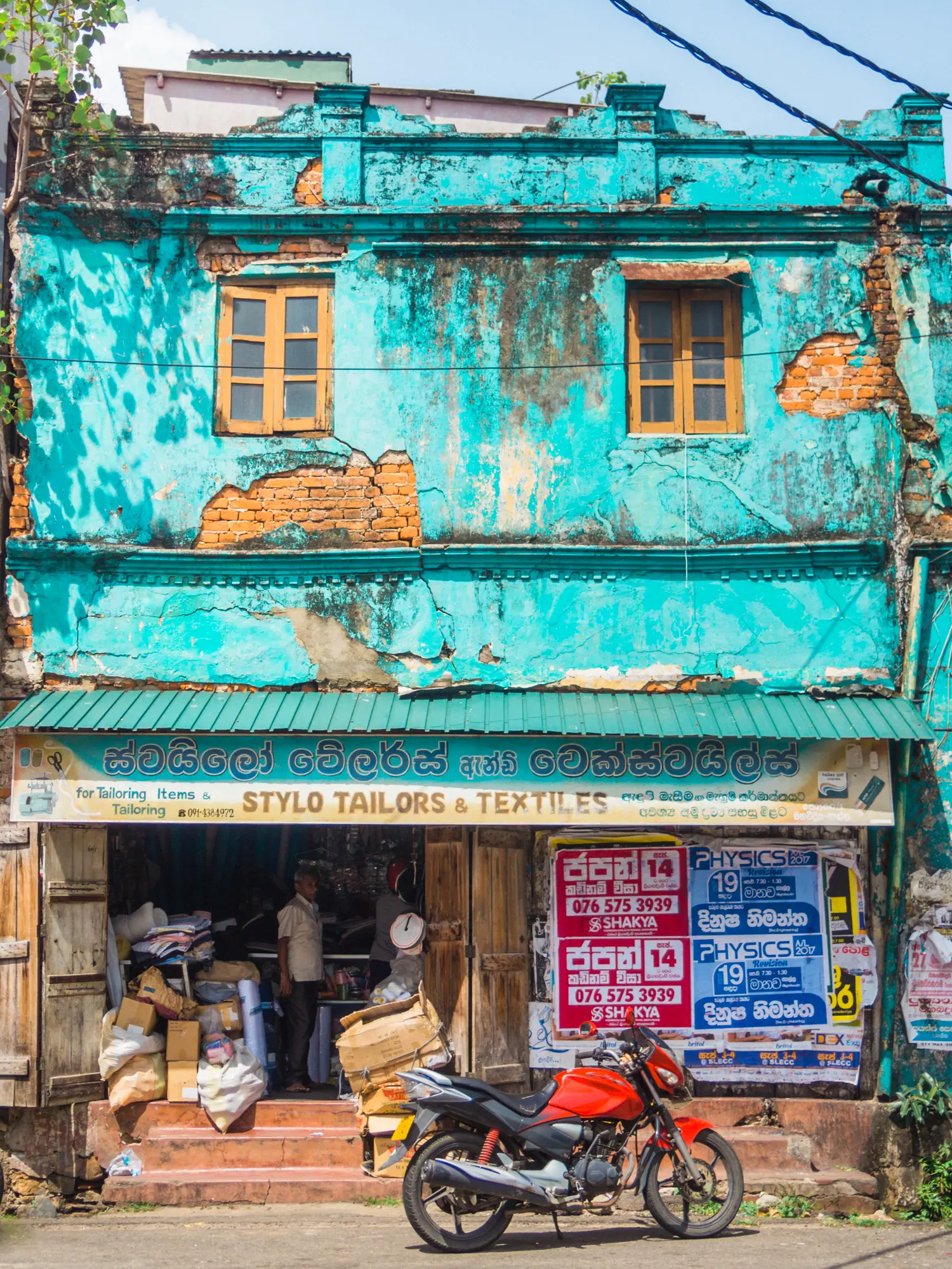 Run down turqouise building with a red motorbike in front in Galle, Unawatuna