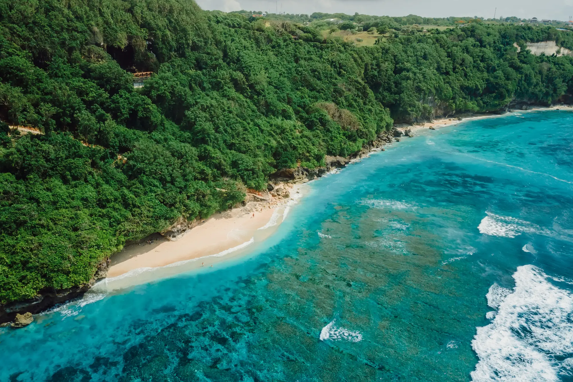 Aerial view of the small Green Bowl Beach surrounded by turquoise water, set at the bottom of a lush cliff in Uluwatu Bali.