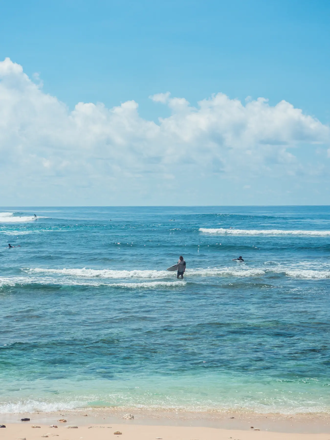 Surfer holding a surfboard walking up from the turquoise water on a sunny day at Green Bowl Beach in Bali.