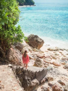 Girl wearing a red kimono walking down the stone stairs at the rocky Green Bowl Beach in Bali.