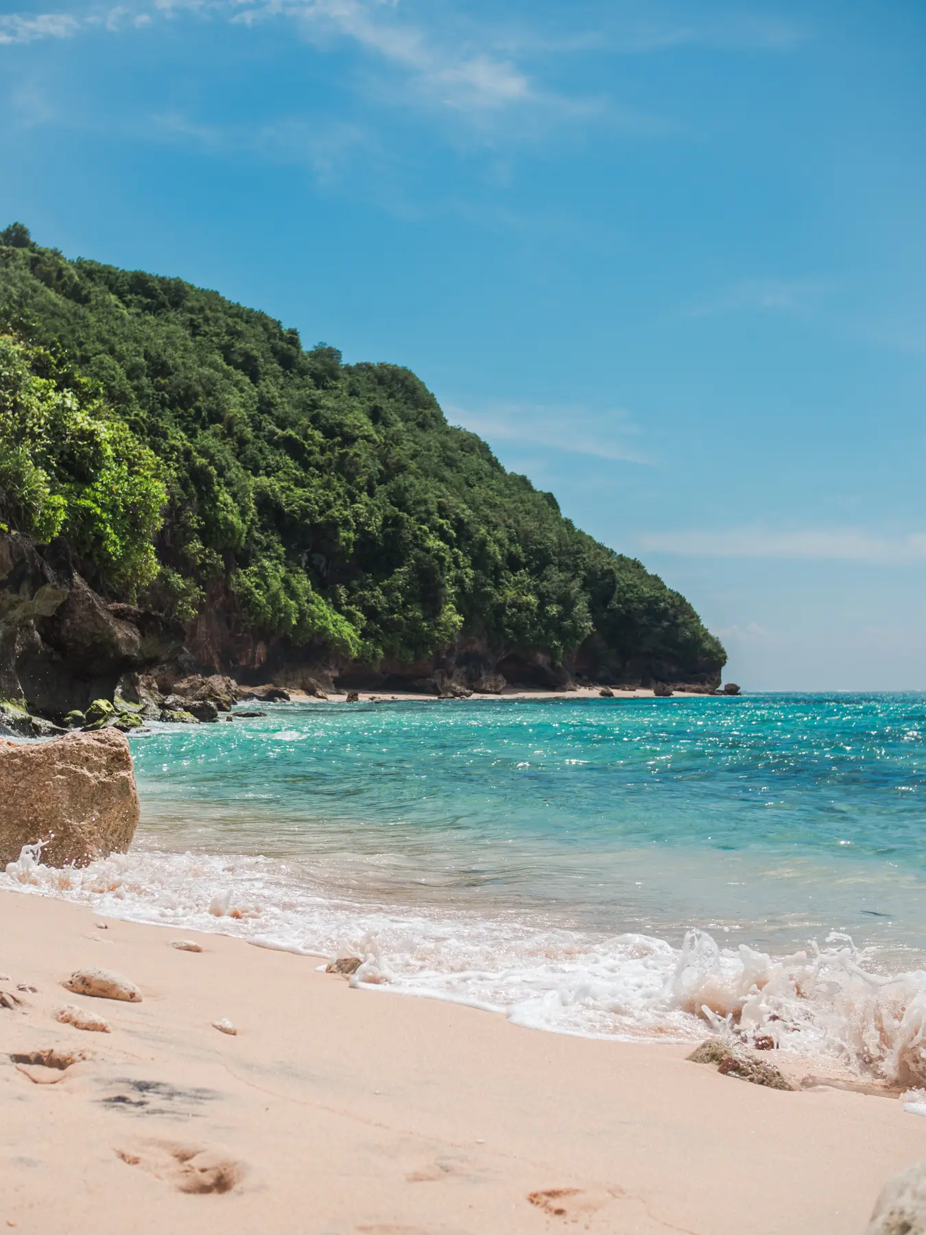 View of the turquoise ocean, with a lush green cliff in the background, from Green Bowl Beach in Bali.
