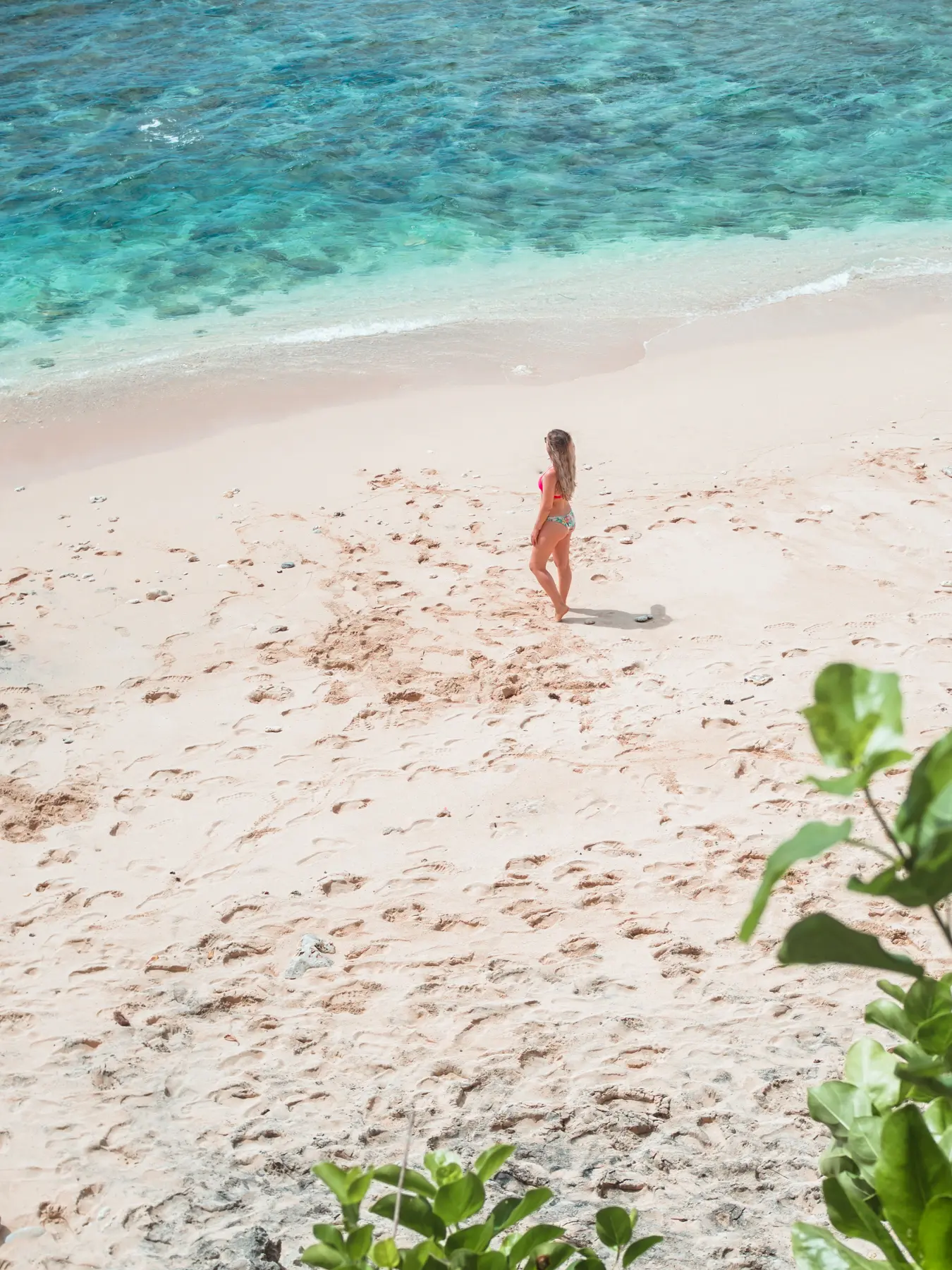 View from above of a girl standing by the turquoise ocean on the light-colored Green Bowl Beach in Bali.