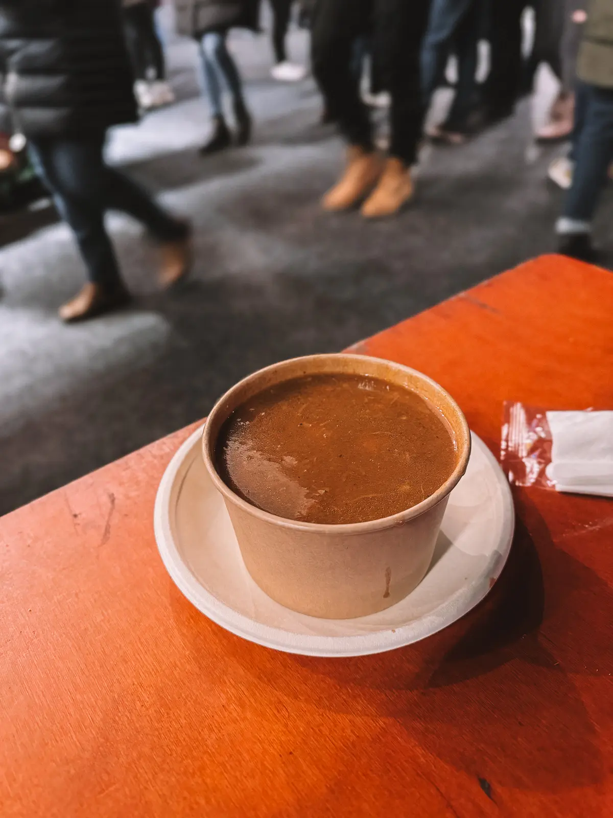 Goulash soup in a paper cup on an orange table, best street food in Budapest.