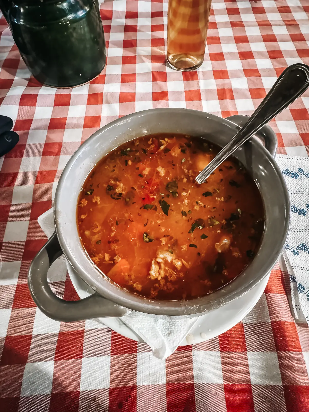 Orange Gulyas soup in a grey bowl on a table with a red and white checkered tablecloth, best street food in Budapest. 