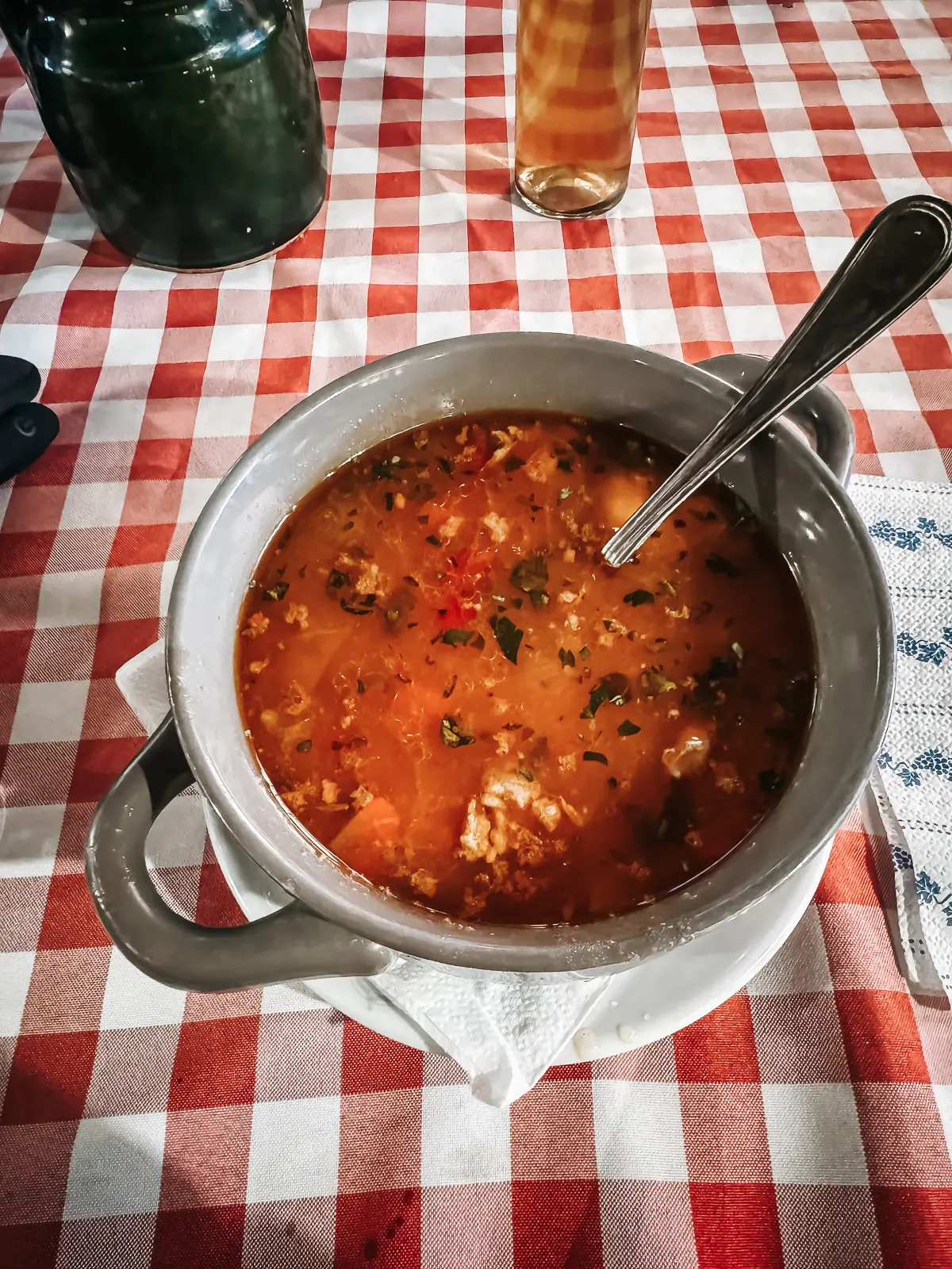 Orange Gulyas soup in a grey bowl on a table with a red and white checkered tablecloth, best street food in Budapest.