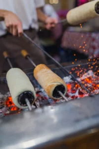 3 Hungarian Chimney Cakes (kurtos kalacs) cooked on spits over coal, best street food in Budapest.