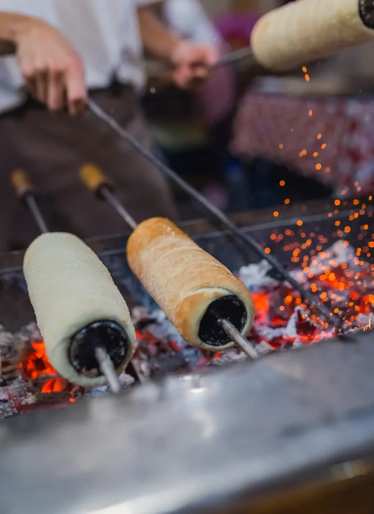 3 Hungarian Chimney Cakes (kurtos kalacs) cooked on spits over coal, best street food in Budapest.