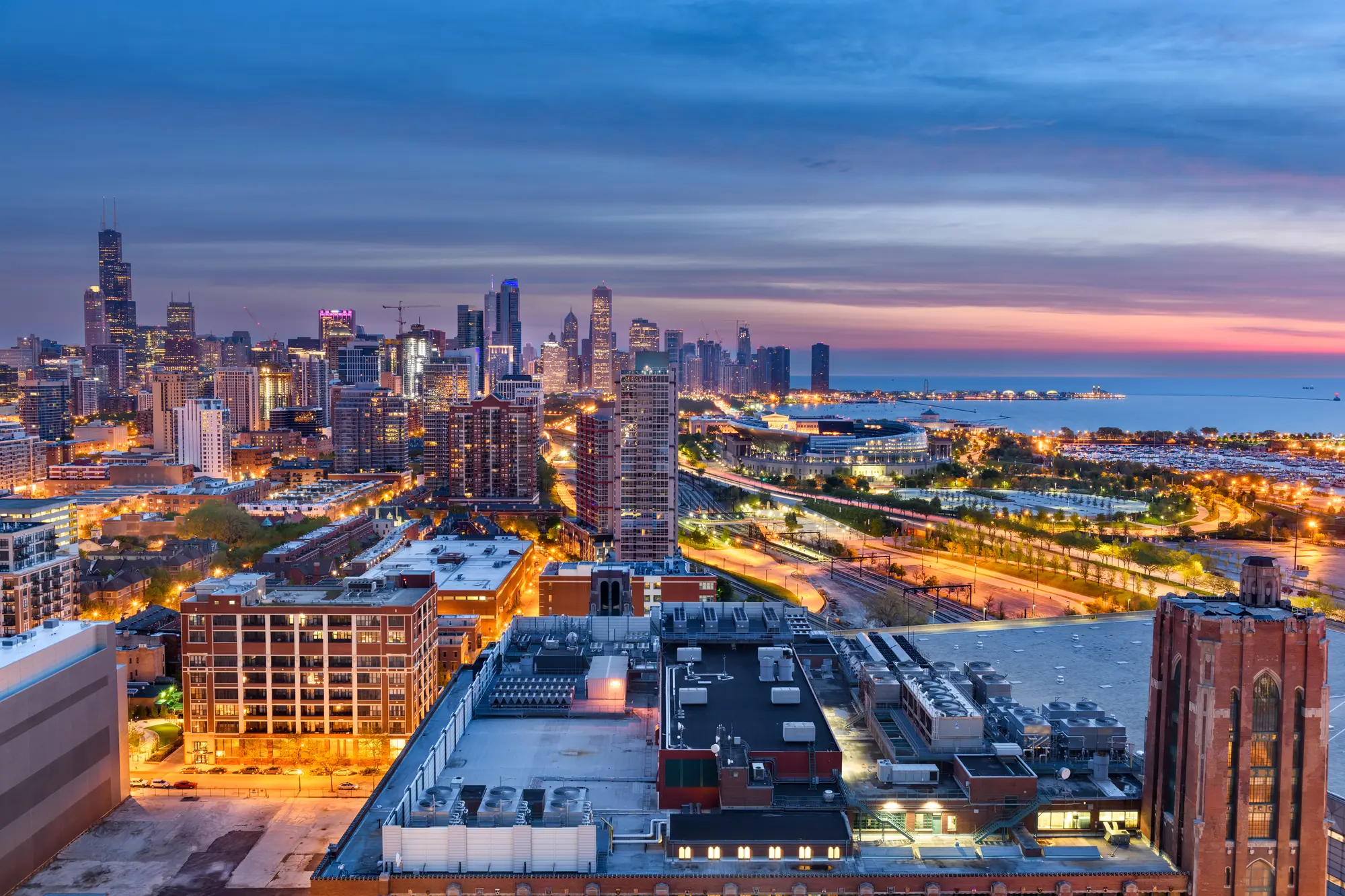 Aerial view of the skyscrapers of Downtown, one of the best areas to stay in Chicago, and the harbor lit up at dusk.
