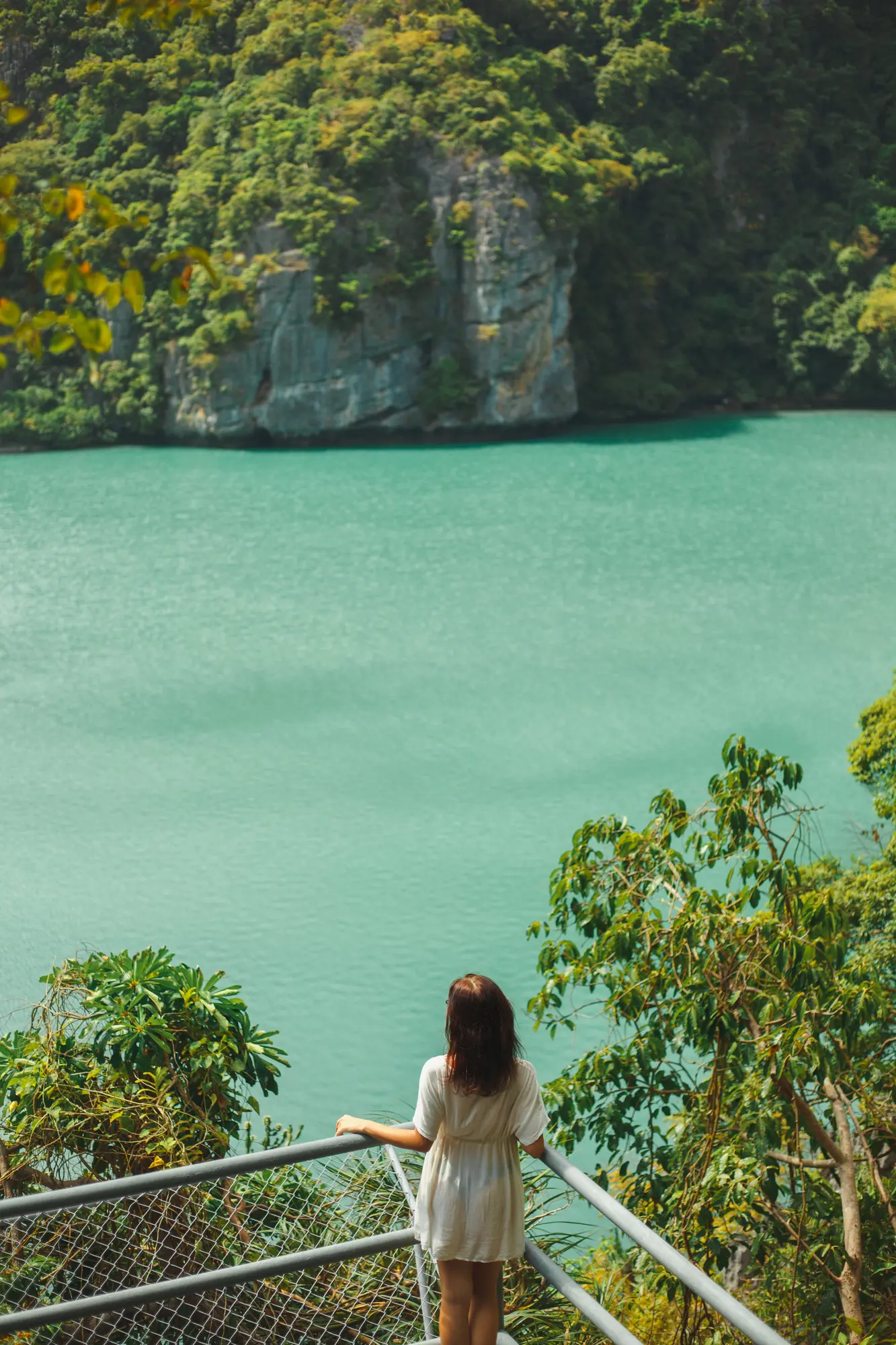 Girl in a white dress standing on a platform looking out over green water in Ang Thong National Marine Park - Thailand vs. Indonesia