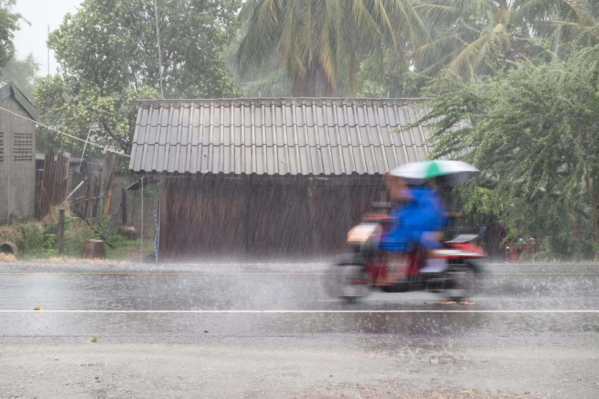 Scooter driving fast in the rain during monsoon season in Thailand vs Indonesia.