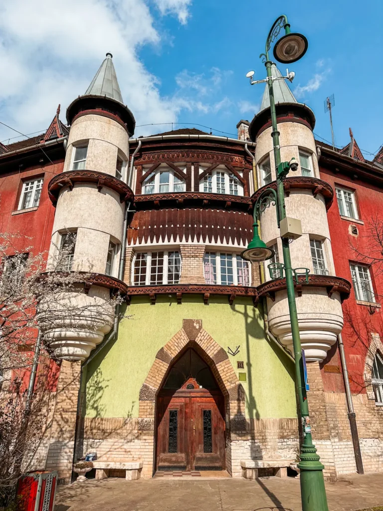Medieval inspired red and green building with two grey towers, wooden features at Wekerletelep, one of the best hidden gems in Budapest Hungary.