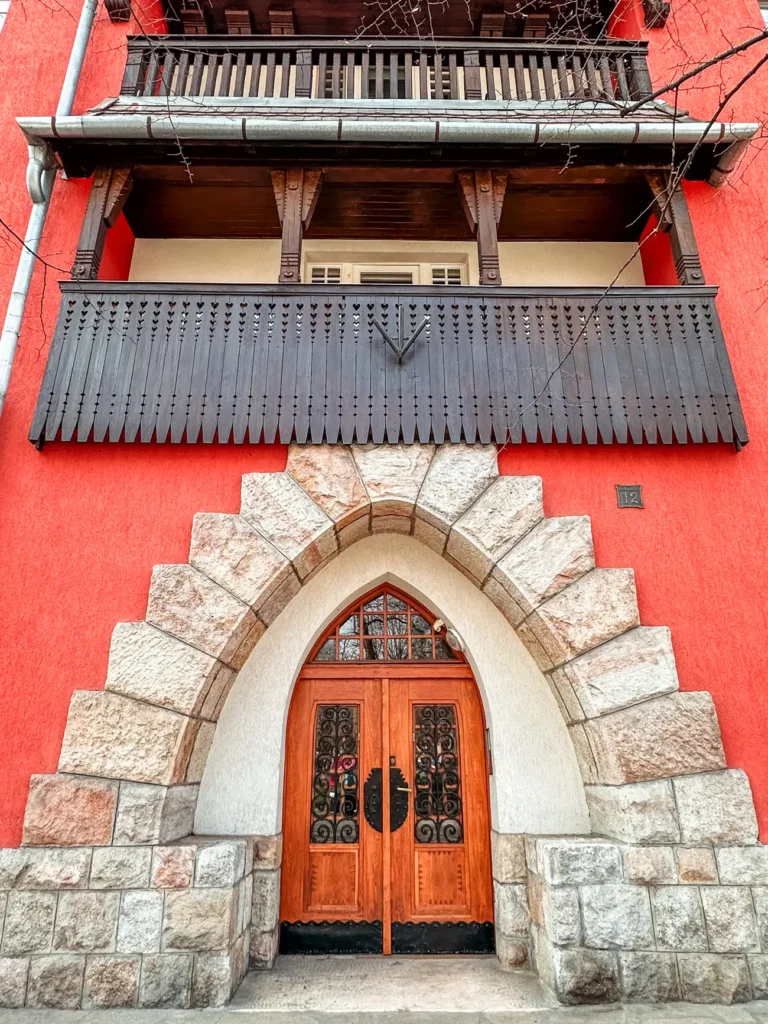 Coral colored stone house with wooden veranda and a stone archway around the door at Wekerletelep, a hidden gem in Budapest.