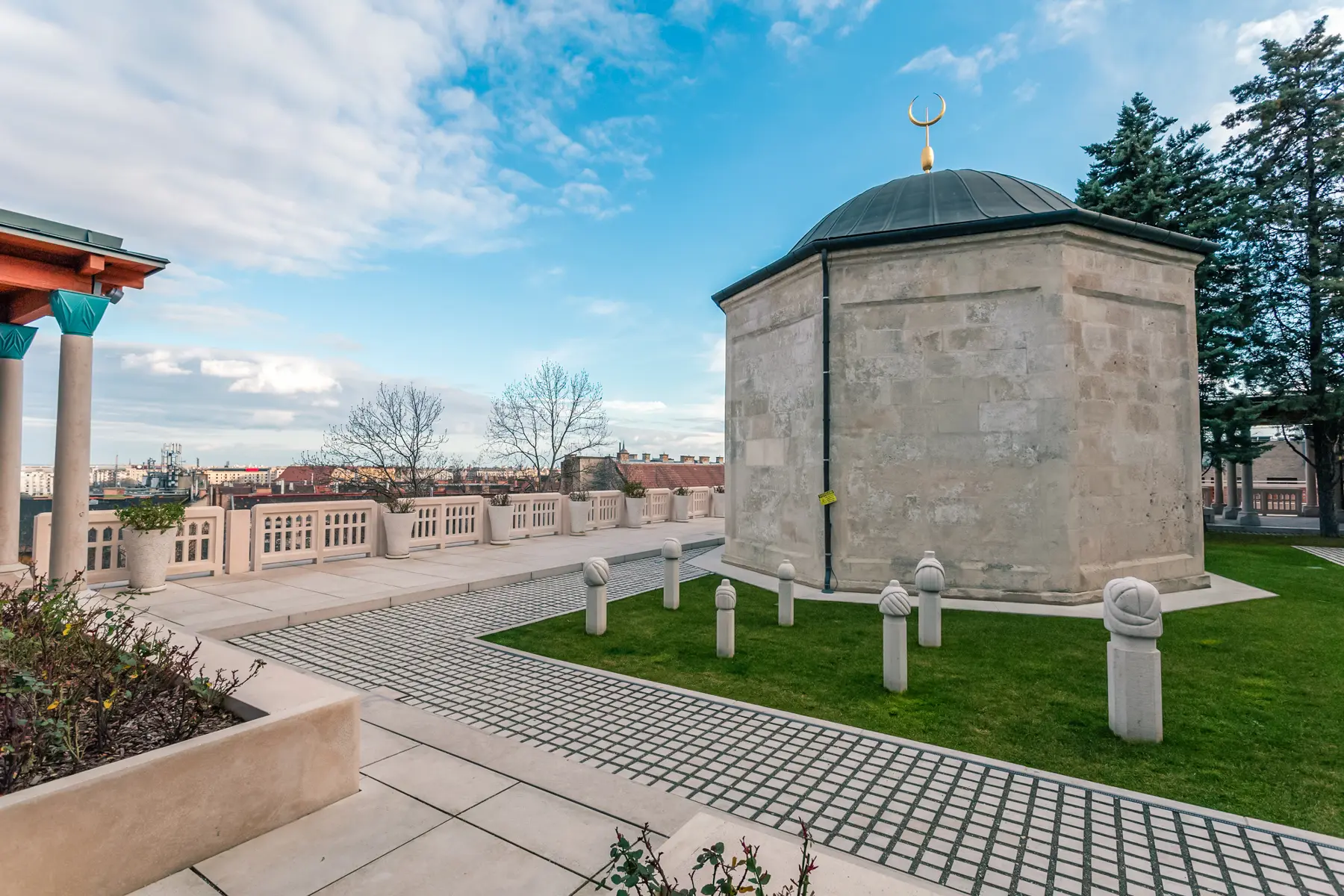 Hexagonal stone building with black roof surrounded by grass and tiles at the Tomb of Gül Baba, a hidden gem in Budapest.