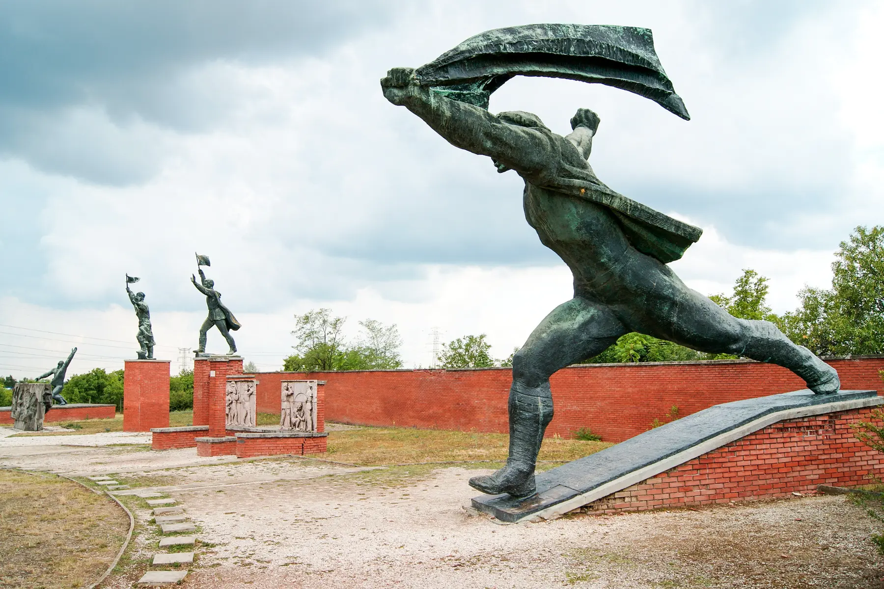 4 Soviet era large statues in Momento Park along a brick wall, a hidden gem in Budapest Hungary.