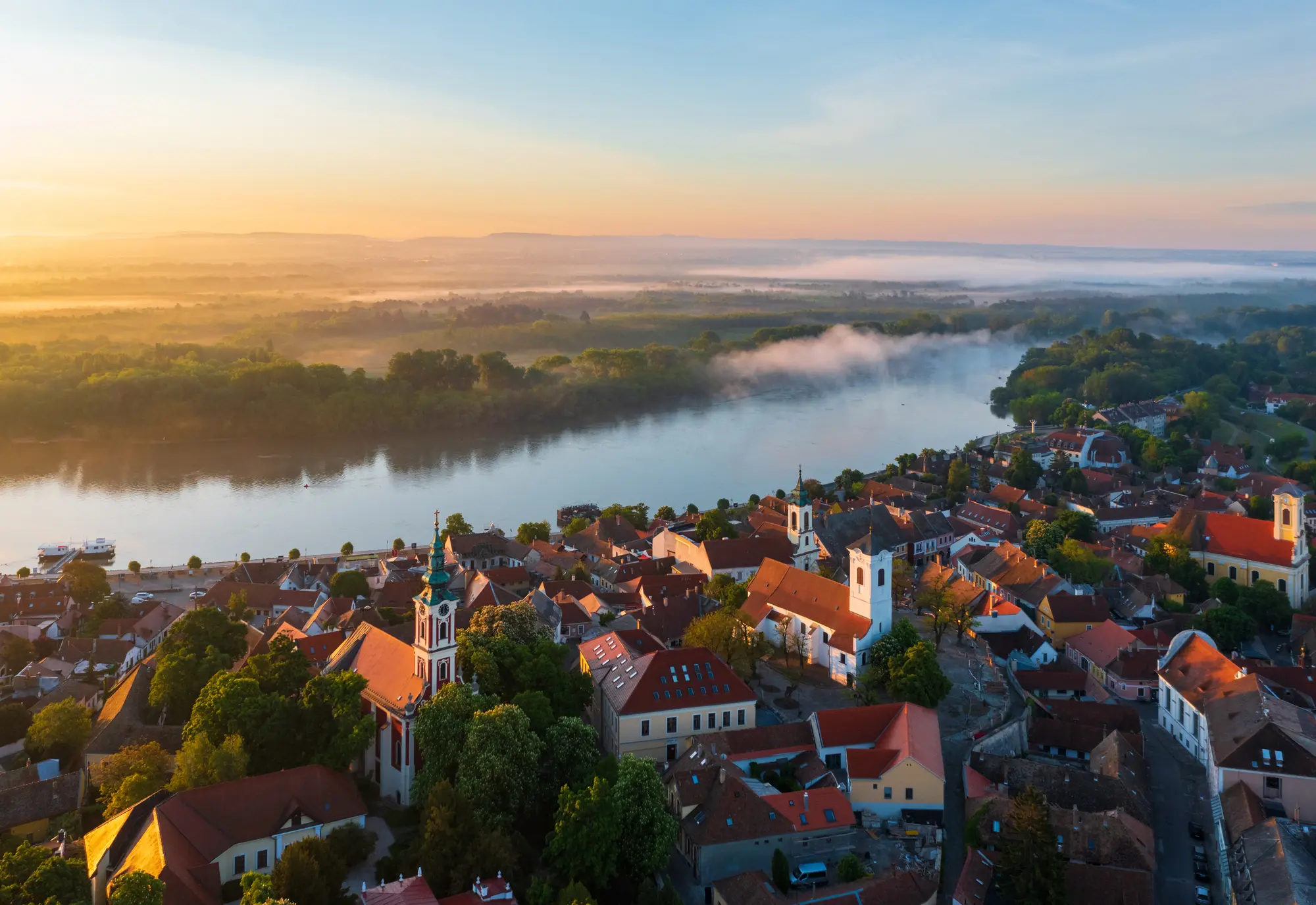 Small town of Szentendre in Hungary set around two white churches with orange roofs by the Danebu river at sunset, a hidden gem near Budapest.