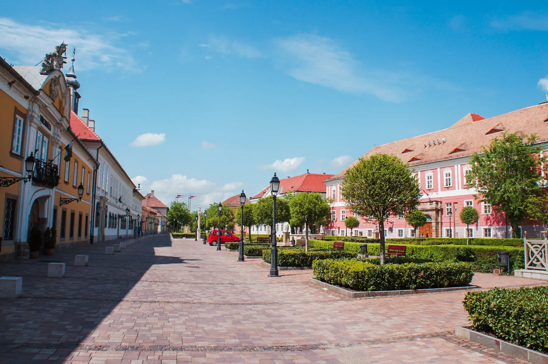 Charming street in Vác with colorful building on both sides, manicured greenery and black street lights, a hidden gem close to Budapest.