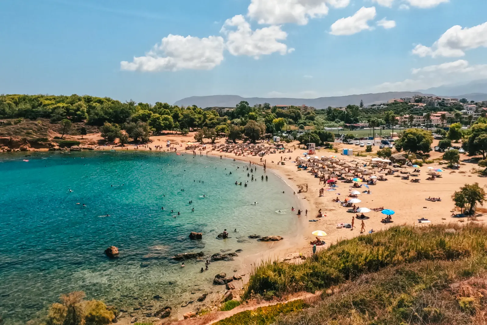 View from a hill on the south side of Agii Apostoli golden bay of sand with two sections of sunbeds and shallow turquoise water, one of the closest beaches to Chania Crete.