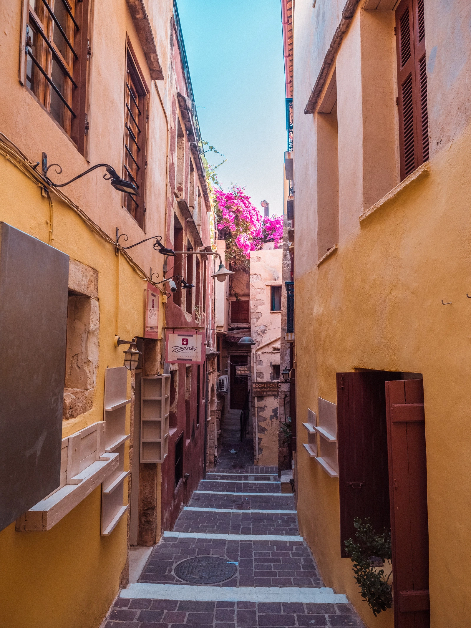 Narrow alley between yellow buildings and pink Bougainvillea flowers, one of the top things to do in Chania after the beach.