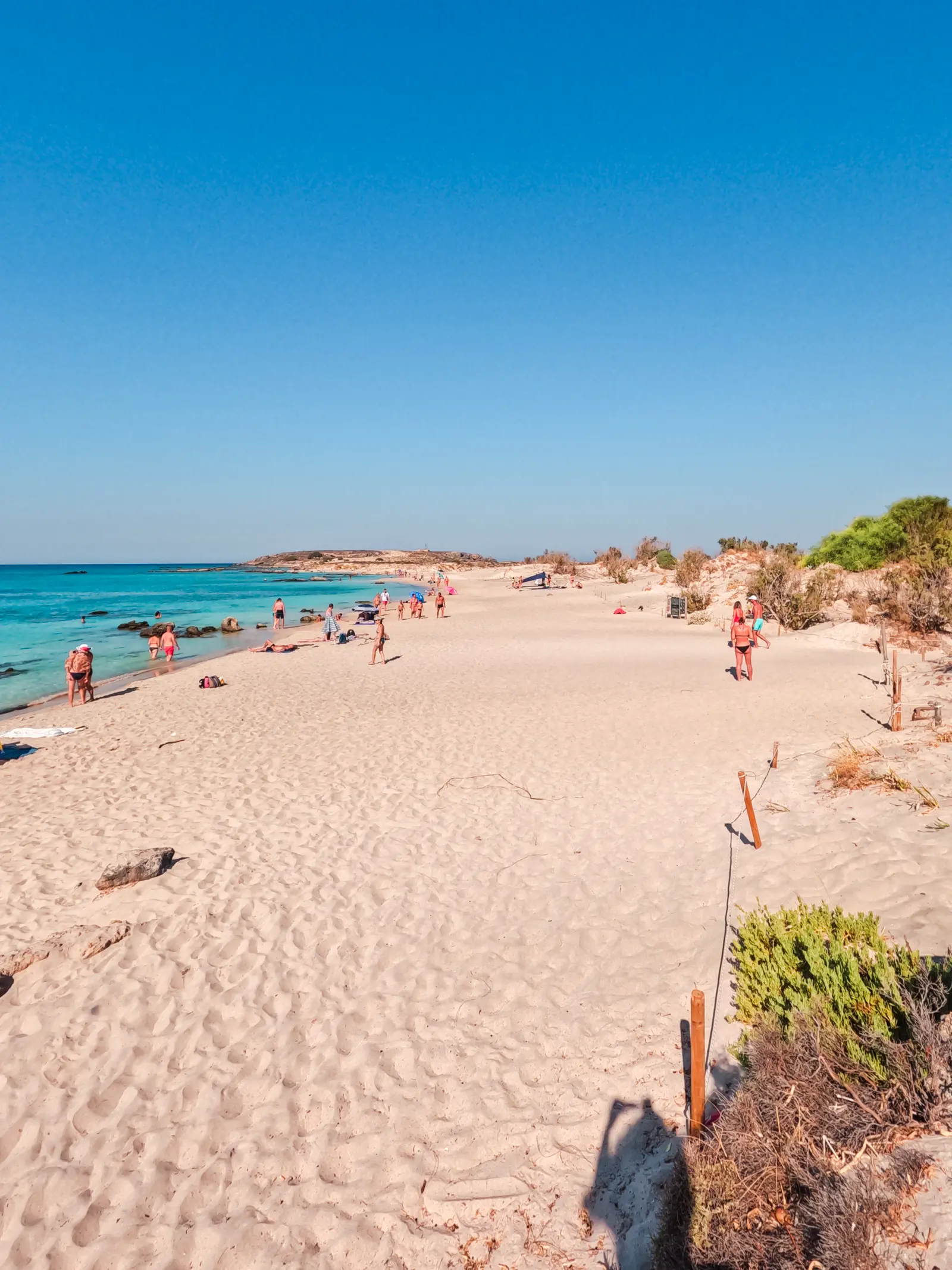 View of people on a light sand beach on Elafonisi Island with blue skies and turquoise water. Chania to Elafonisi Beach.