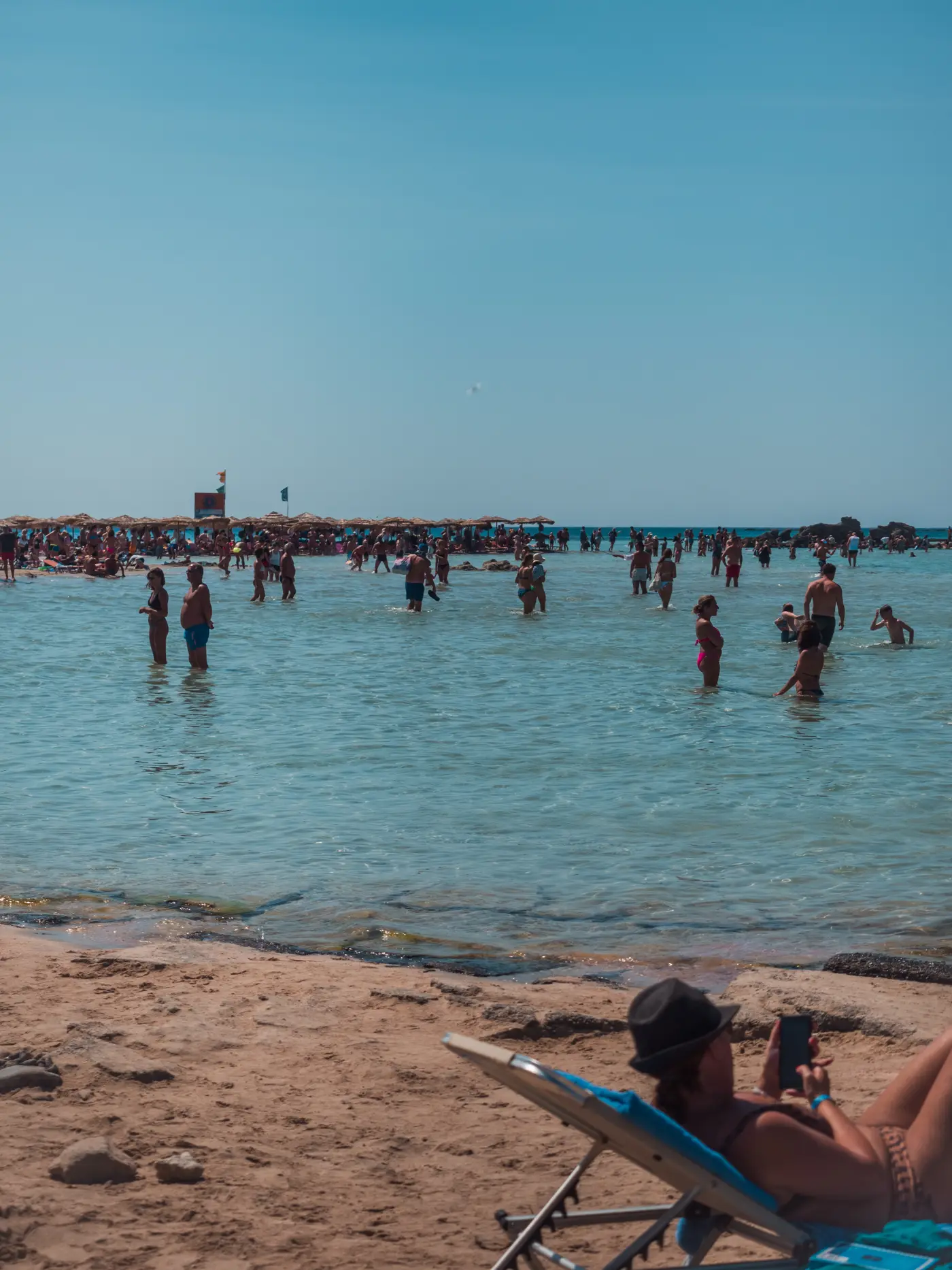 Crowds of people standing out in the shallow water at Elafonisi Beach on a sunny day in late August.
