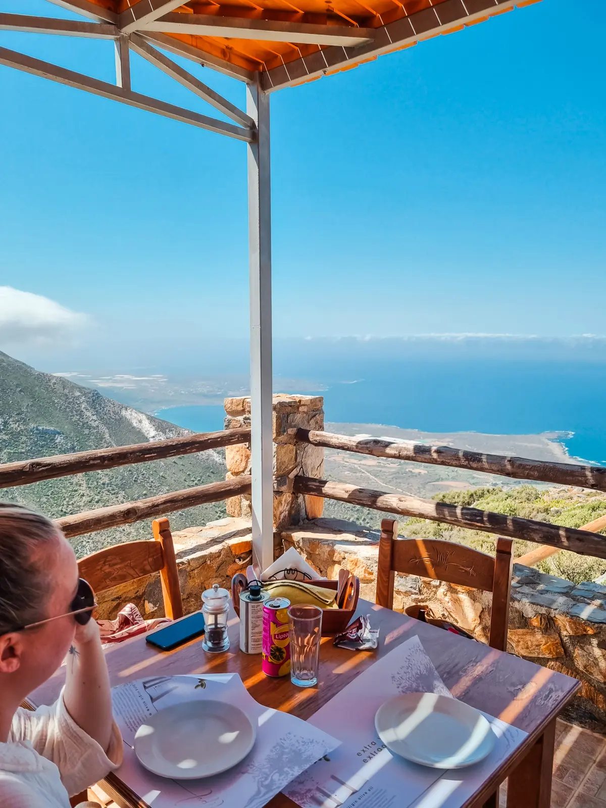 Woman sitting at a table on a cliffside restaurant looking out over the ocean on the way from Falasarna to Elafonisi Beach in Crete.