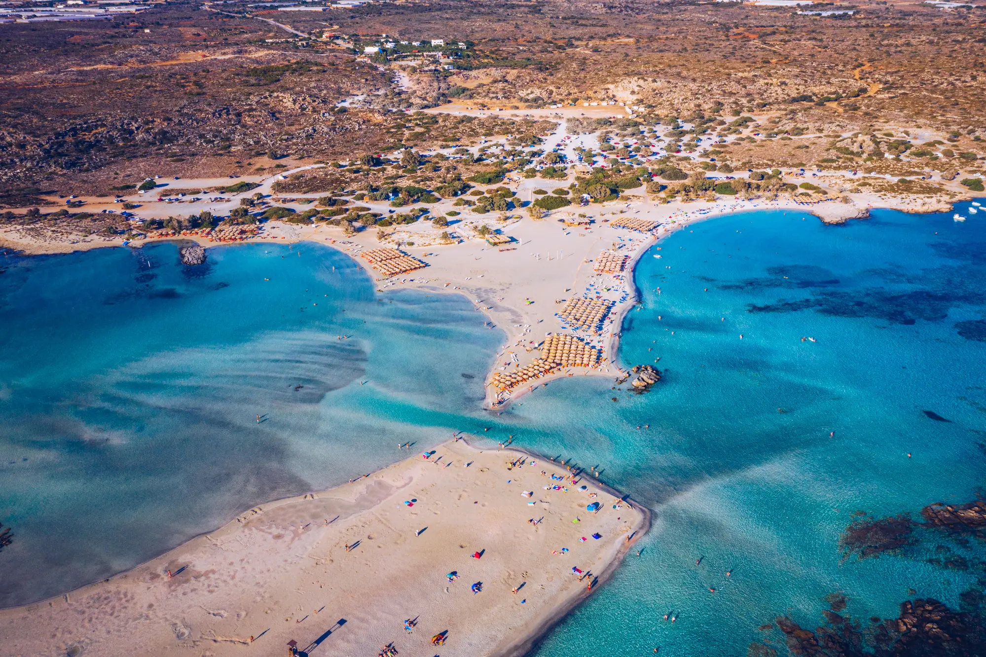 Aerial view of the turquoise shallow water, light beige sand and different areas with sunbeds at Elafonisi Beach in Crete.