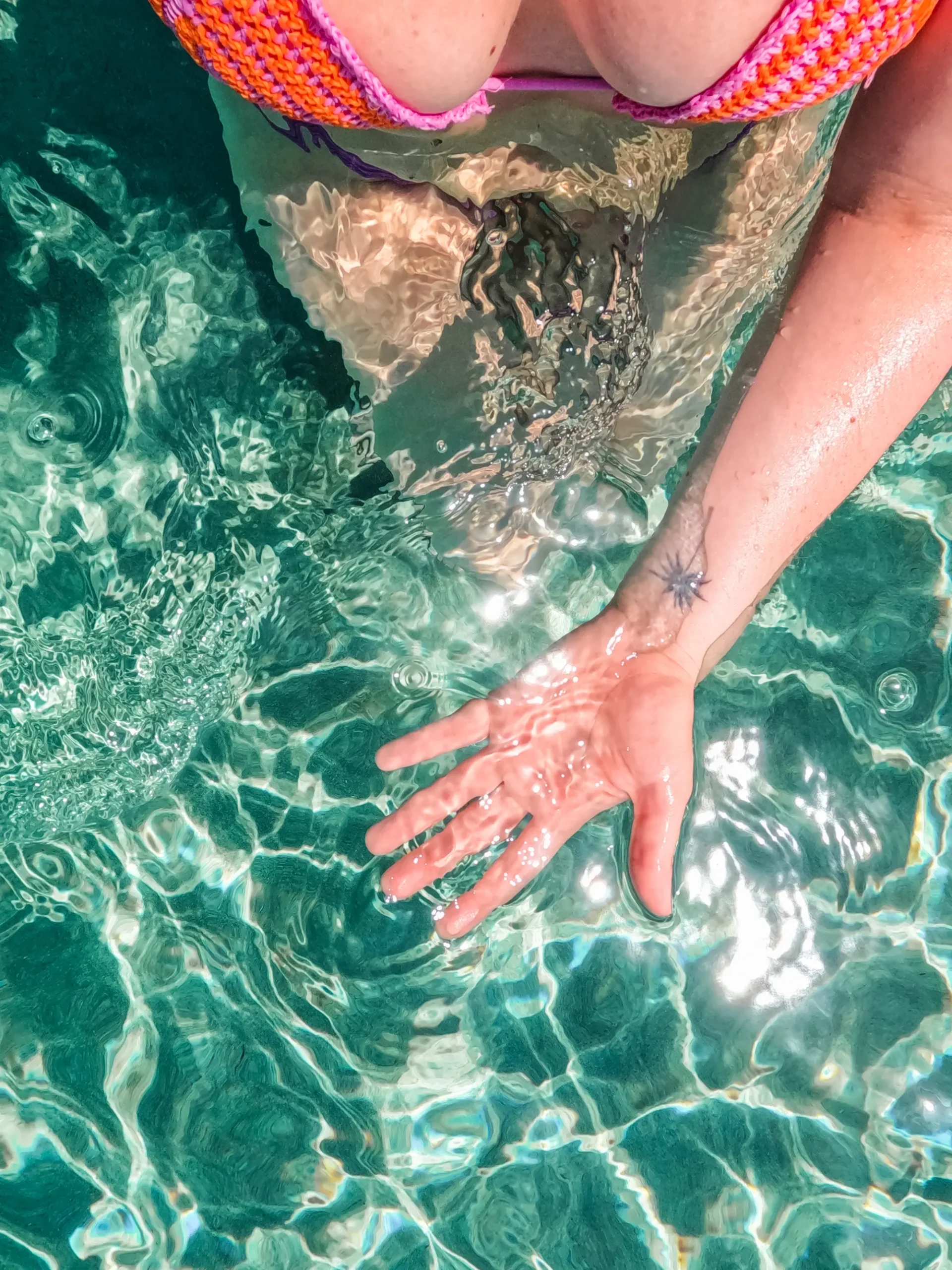 Hand with a palm tree tattoo under the turquoise glistening ocean at Elafonisi Beach in Crete.