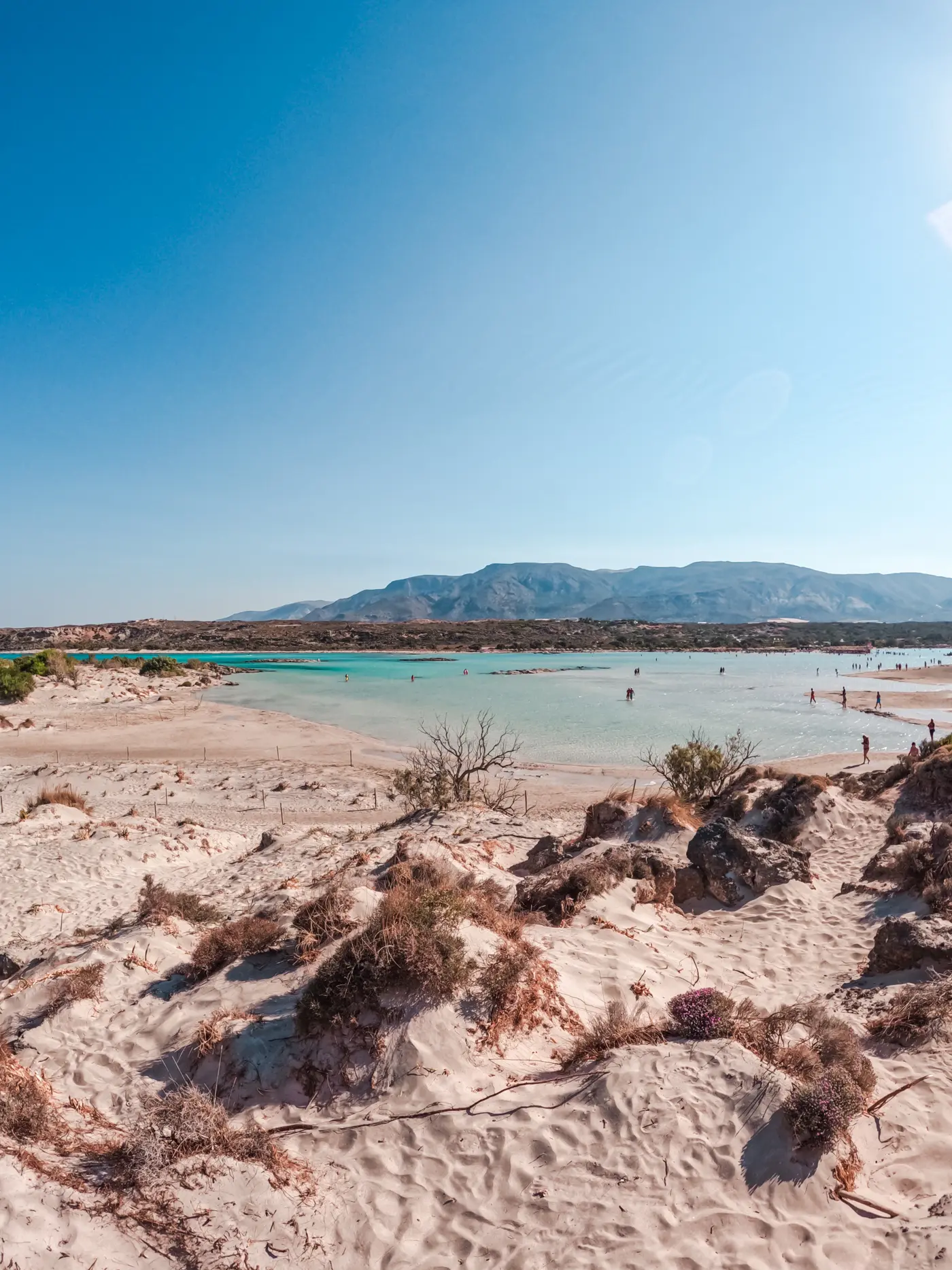 View of light beige sand and a shallow turquoise lagoon with a mountain in the background at Elafonissi Beach in Crete.