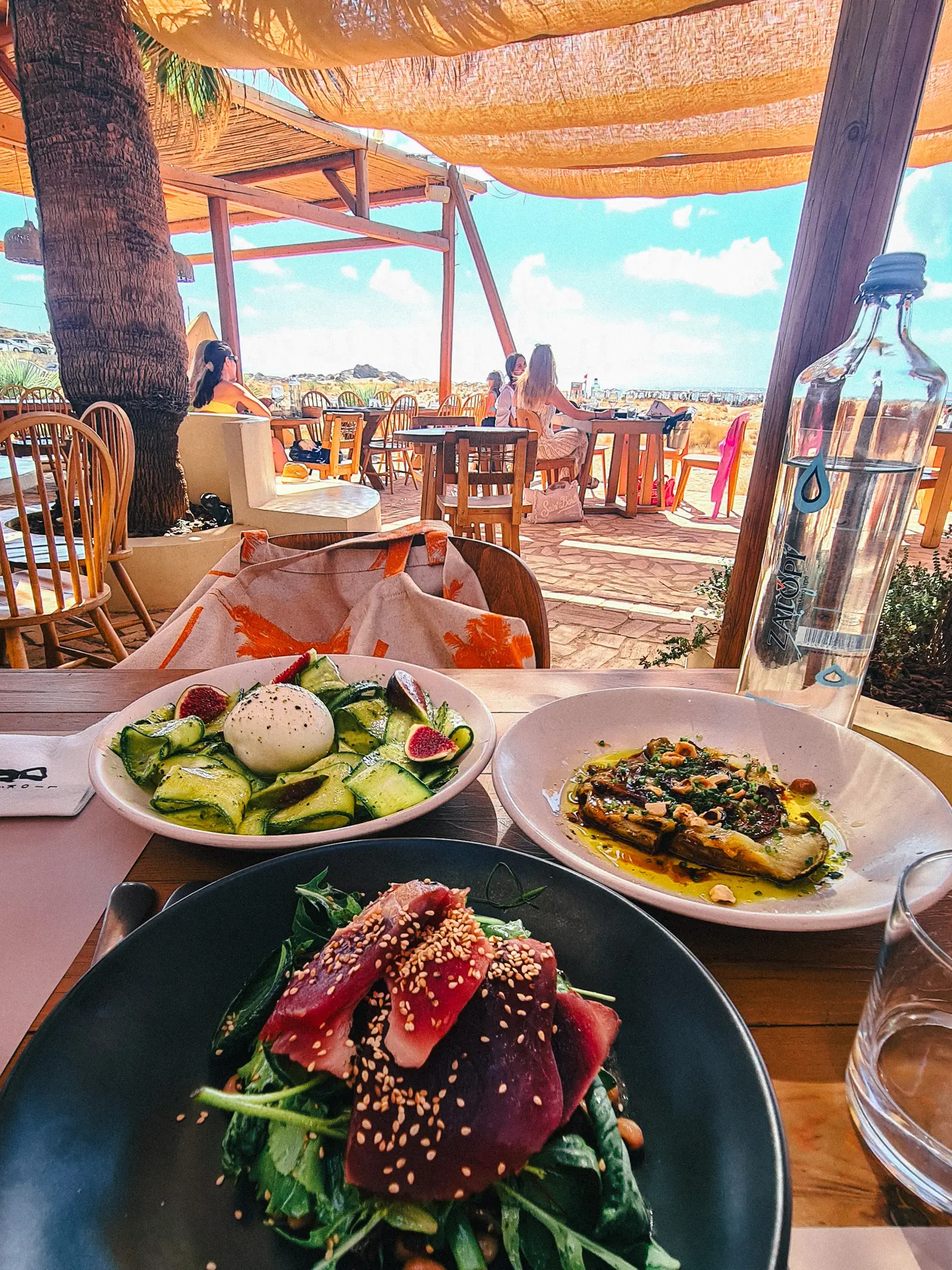 Tuna filet on greens on a black plate, white plate with zucchini salad and burrata, white plate with eggplant on a table in Liokalyvo Beach House Taverna at Falassarna Beach.