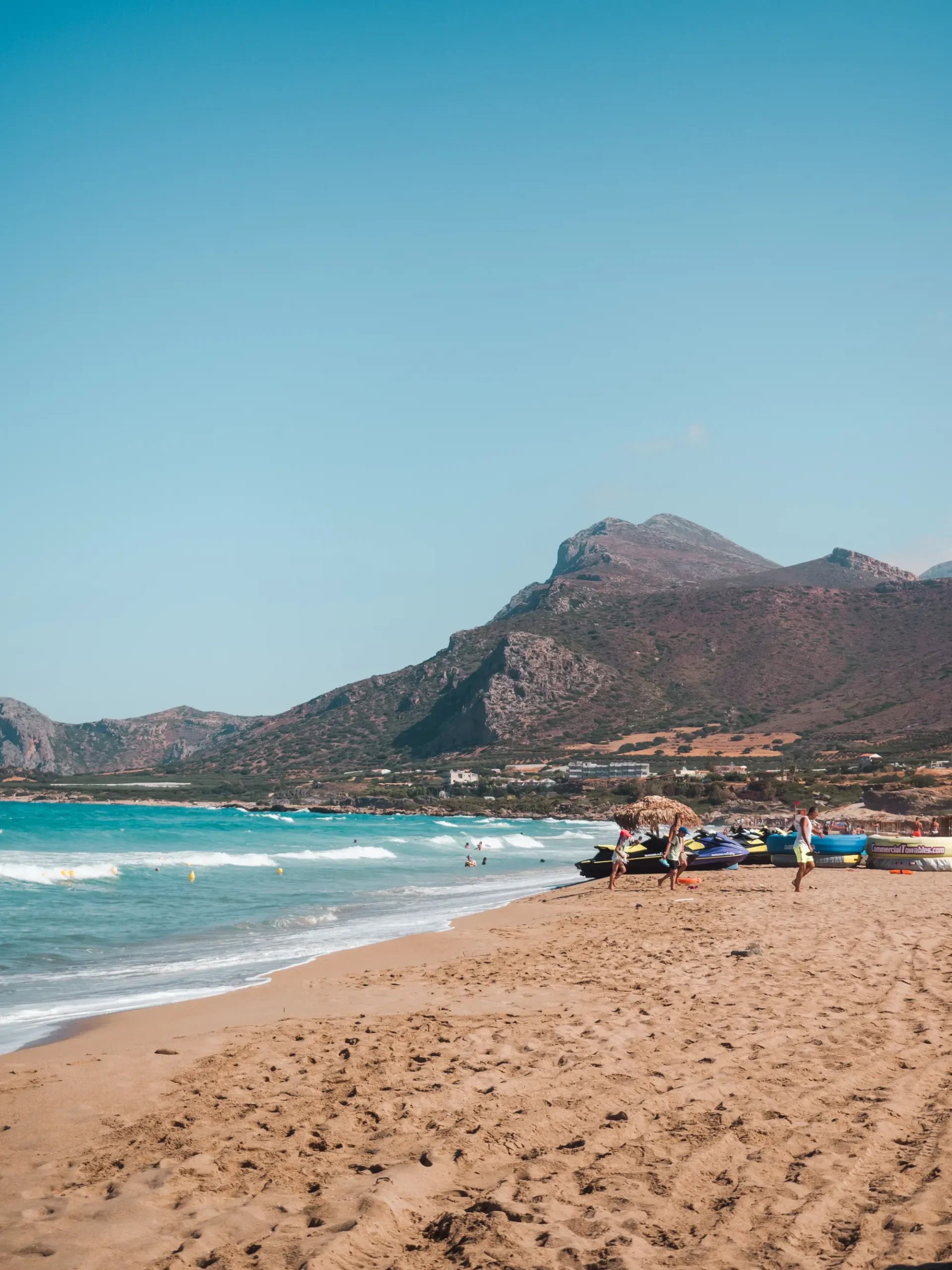 Golden beach and turquoise water with mountains in the background at Falassarna Beach, one of the best beaches in Crete.