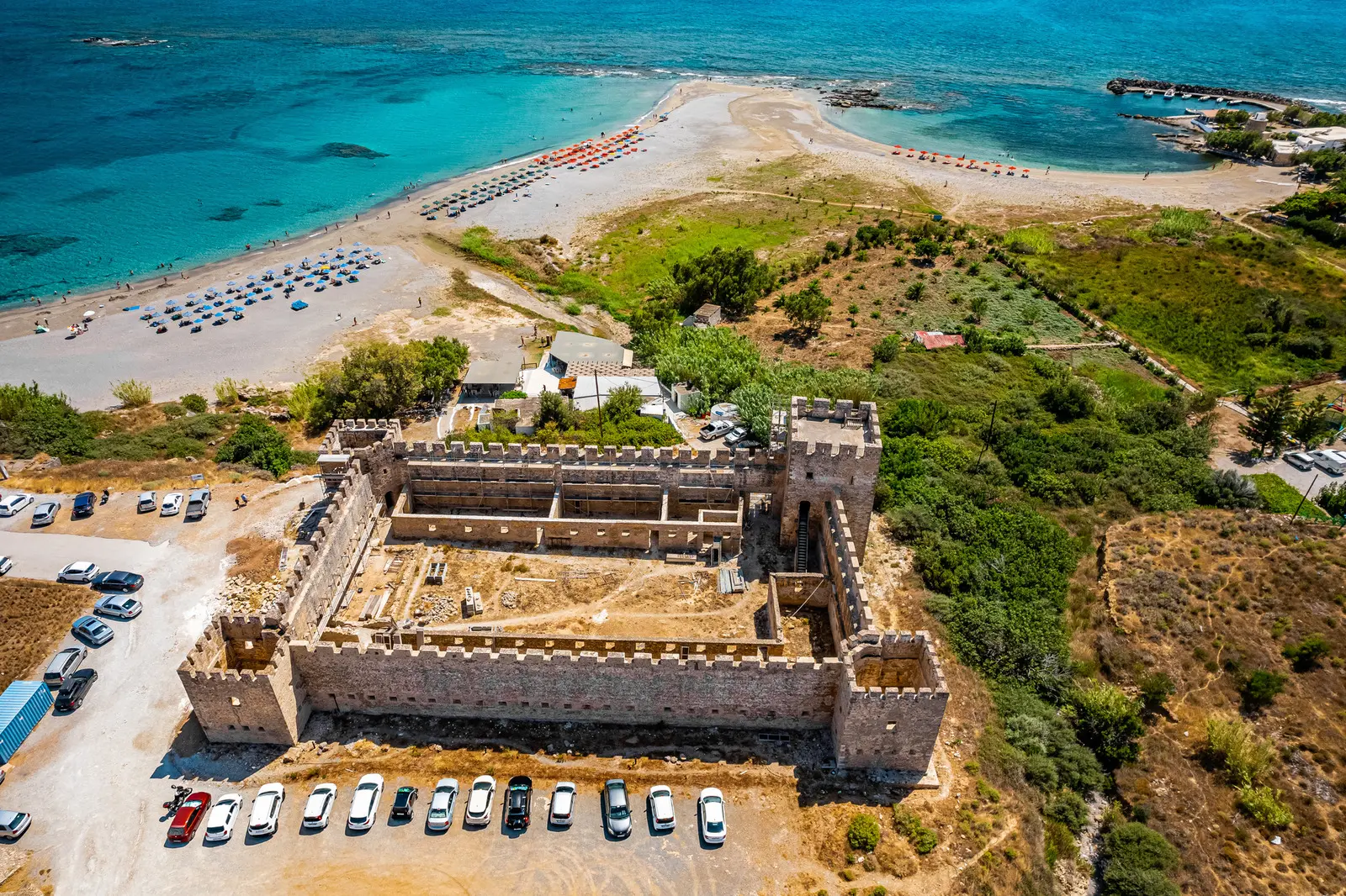 Aerial view of cars parked  around an old stone fortress next to Frangokastello Beach in Chania Crete.