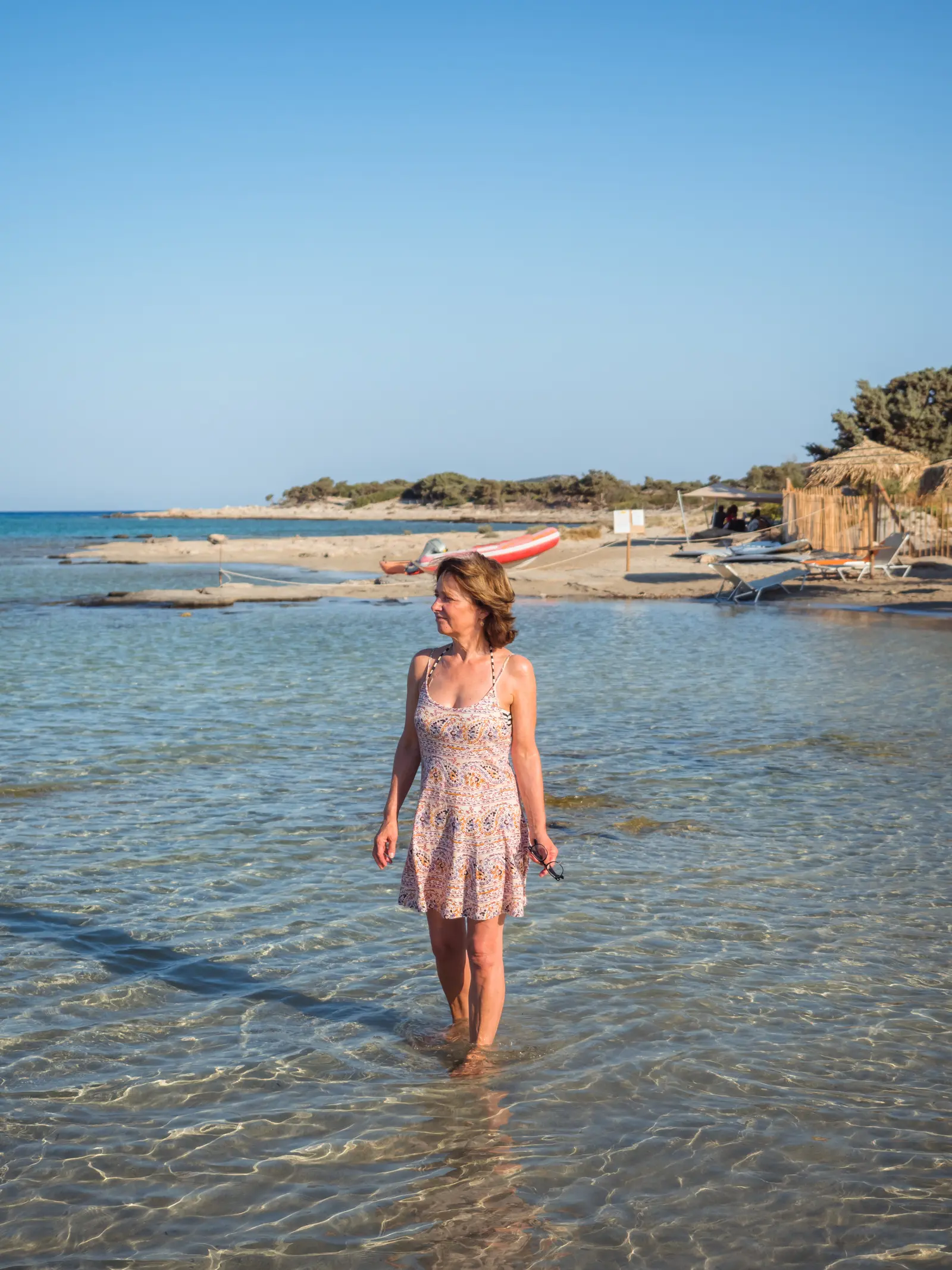 Woman in a beige summer dress standing in the shallow water of Elafonisi Lagoon on a sunny day. Chania to Elafonisi Beach.