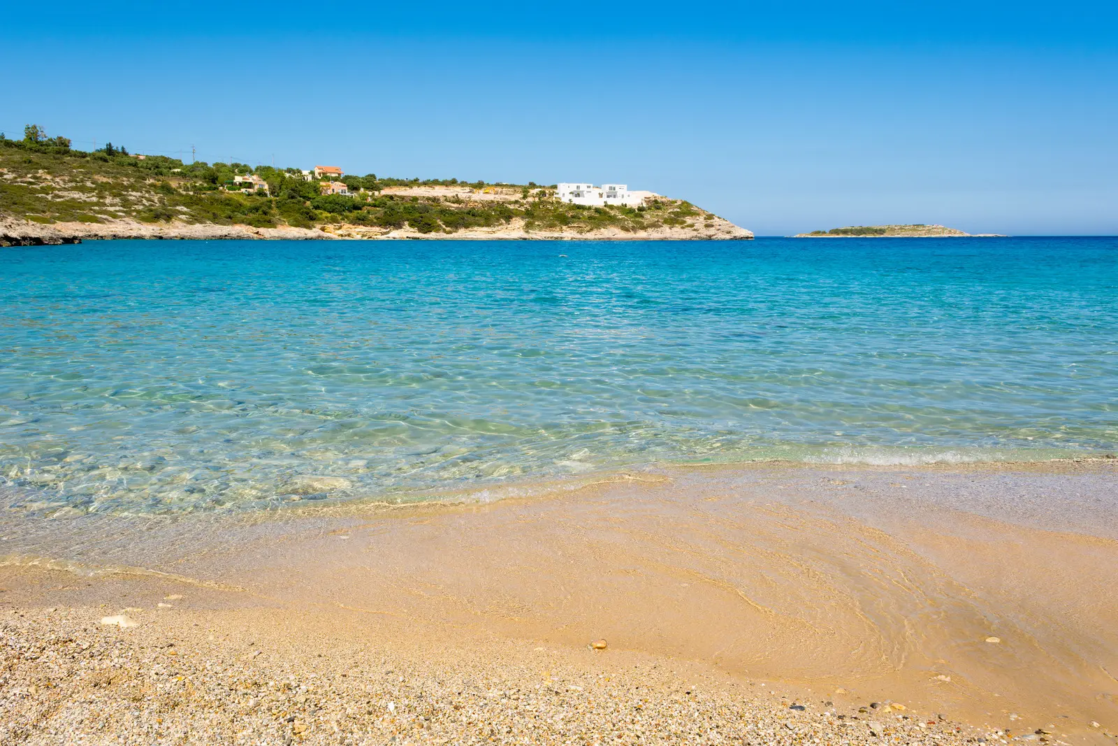 Golden sand and shallow turquoise water with a green headland in the background, Marathi Beach Chania