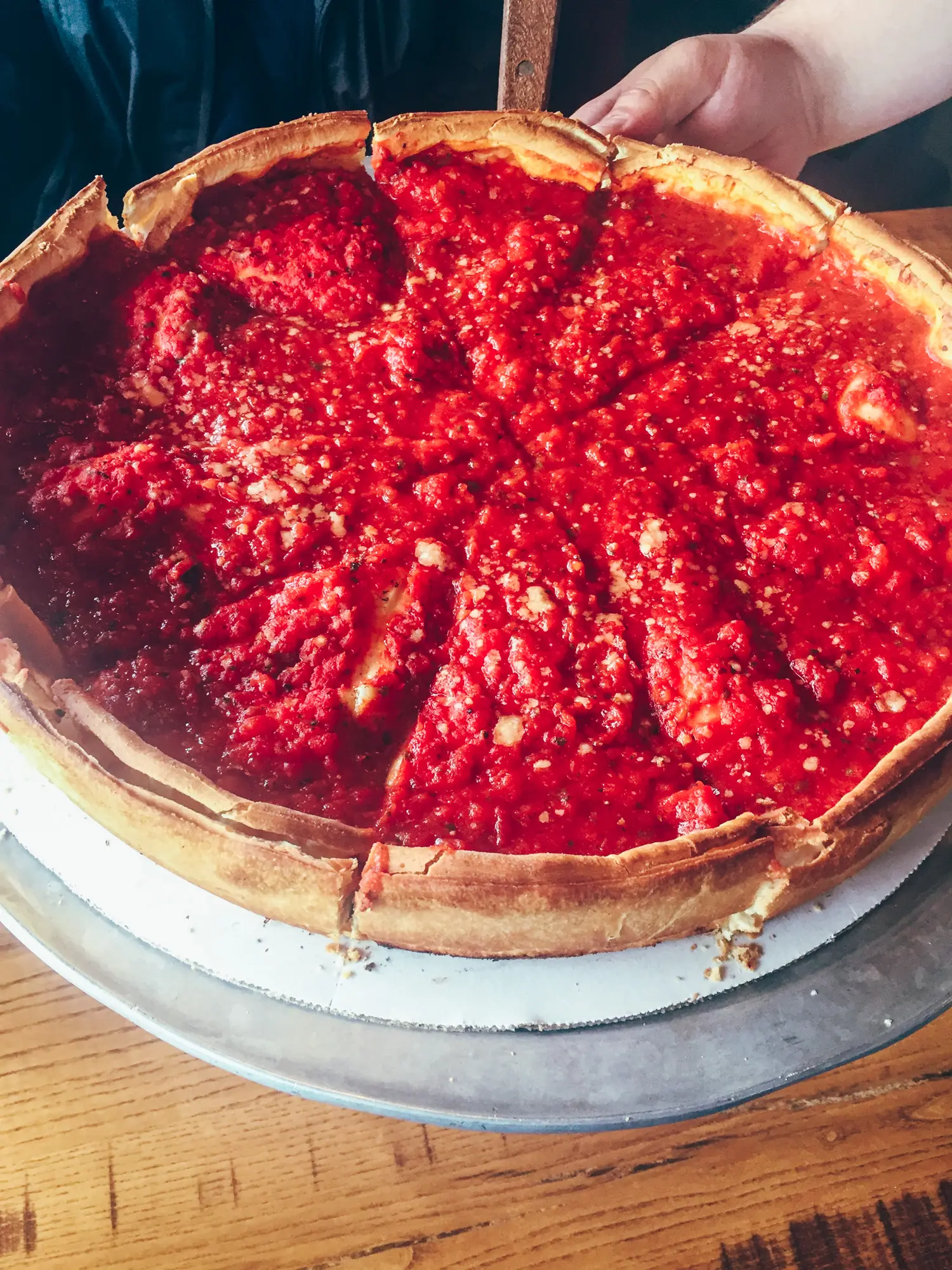 Chicago style deep dish pizza topped with tomato sauce on a metal plate cut into 10 pieces, a must during your weekend in Chicago.