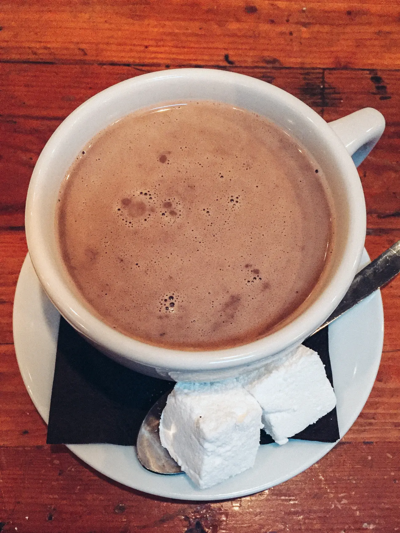 White cup of hot chocolate with two homemade marshmallows on the side at Mindy's Bakery, one of the top things to experience on a weekend in Chicago.