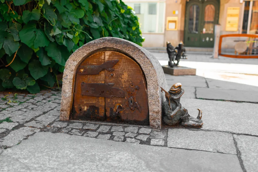 Small metal statue of a dwarf sitting outside his little house on the street in Wroclaw Poland.