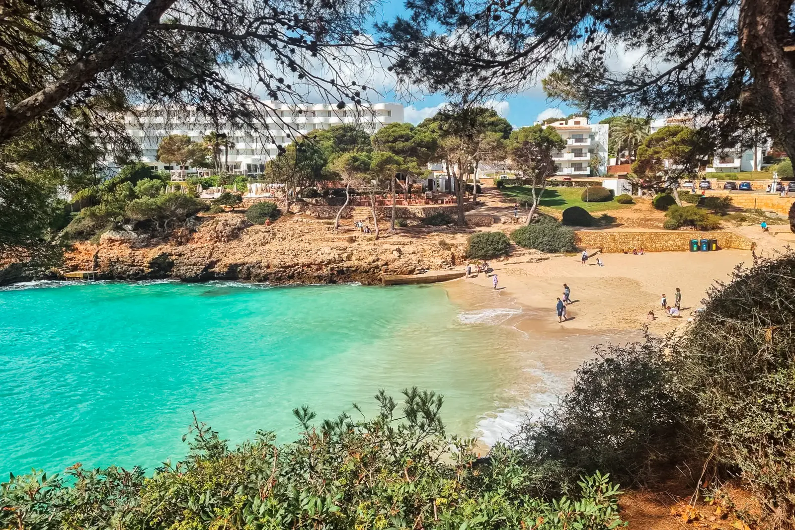 White Inturotel Hotel with rounded verandas looking out over the turquoise ocean of Cala Esmeralda surrounded with pine trees in Mallorca.