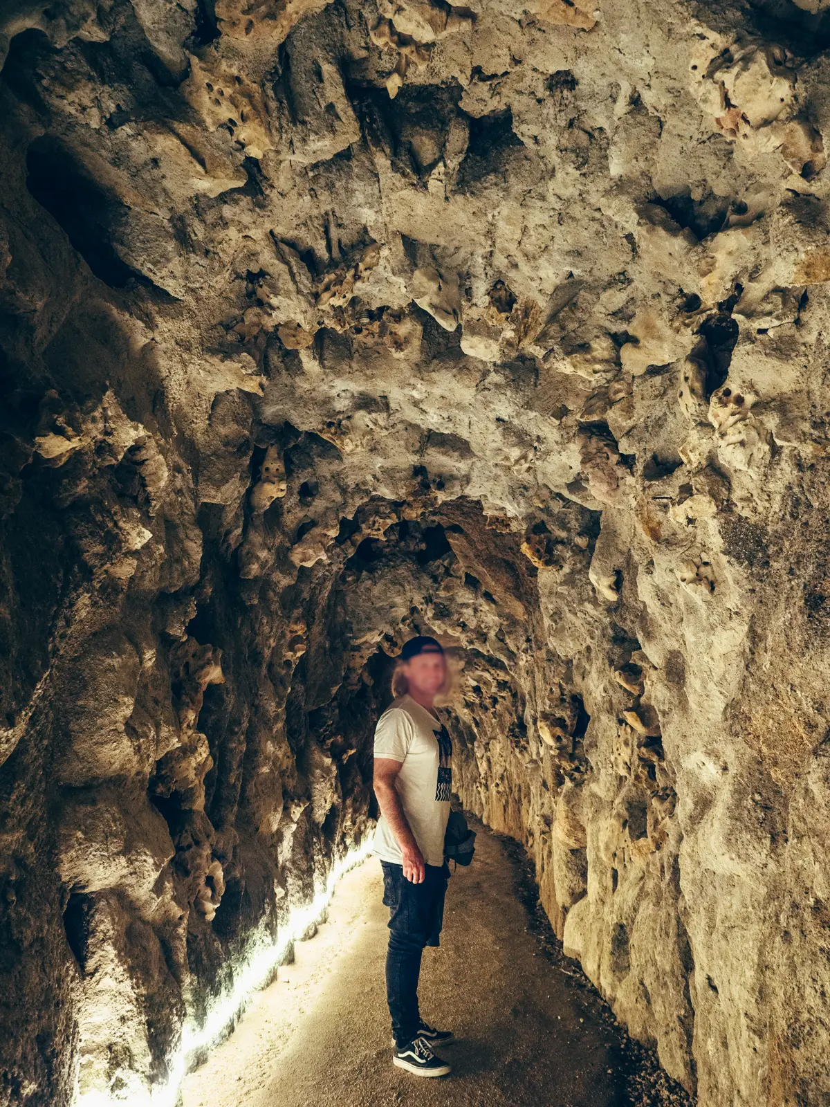 Man in a white t-shirt and black pants walking though a stone tunnel under Quinta da Regaleira.