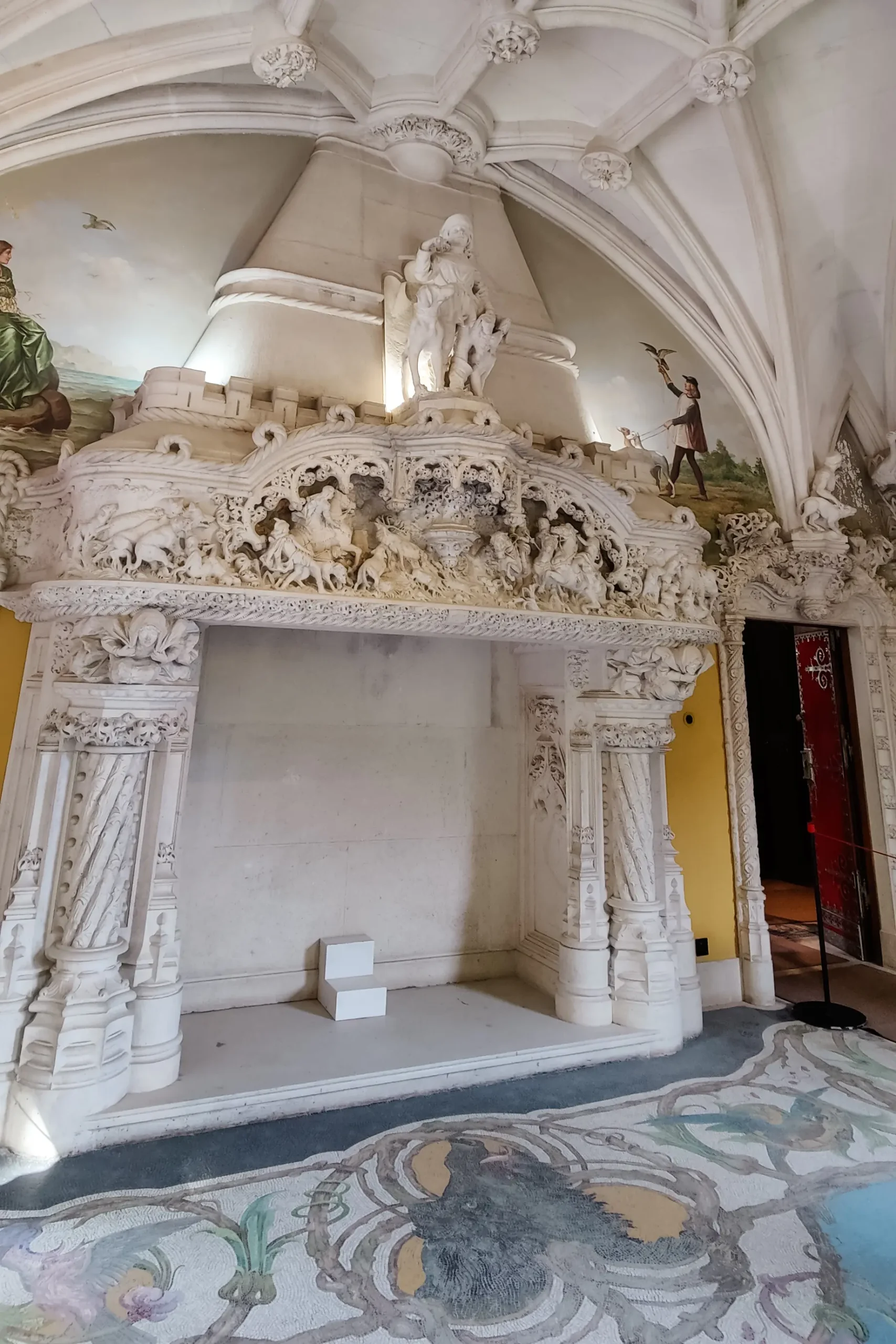 A large white stone fireplace decorated with Gothic style battle scene inside Quinta da Regaleira Palace.