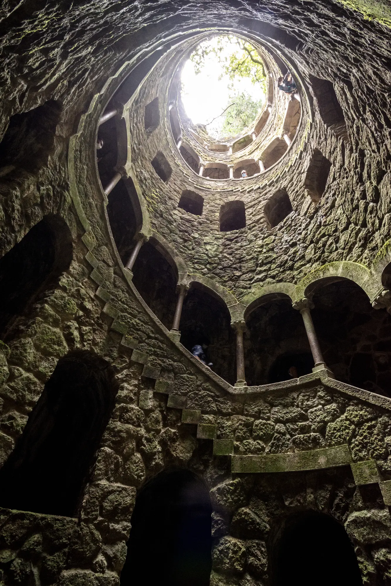 Looking from the bottom up in the stone initiation well at Quinta da Regaleira, with a staircase and arches running up it. 