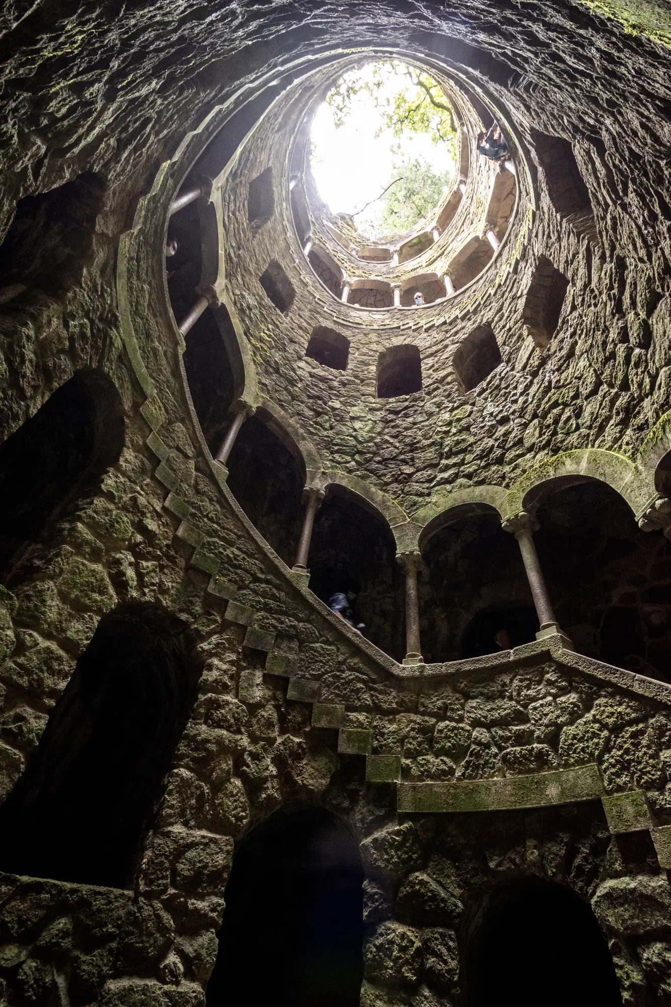 Looking from the bottom up in the stone initiation well at Quinta da Regaleira, with a staircase and arches running up it.