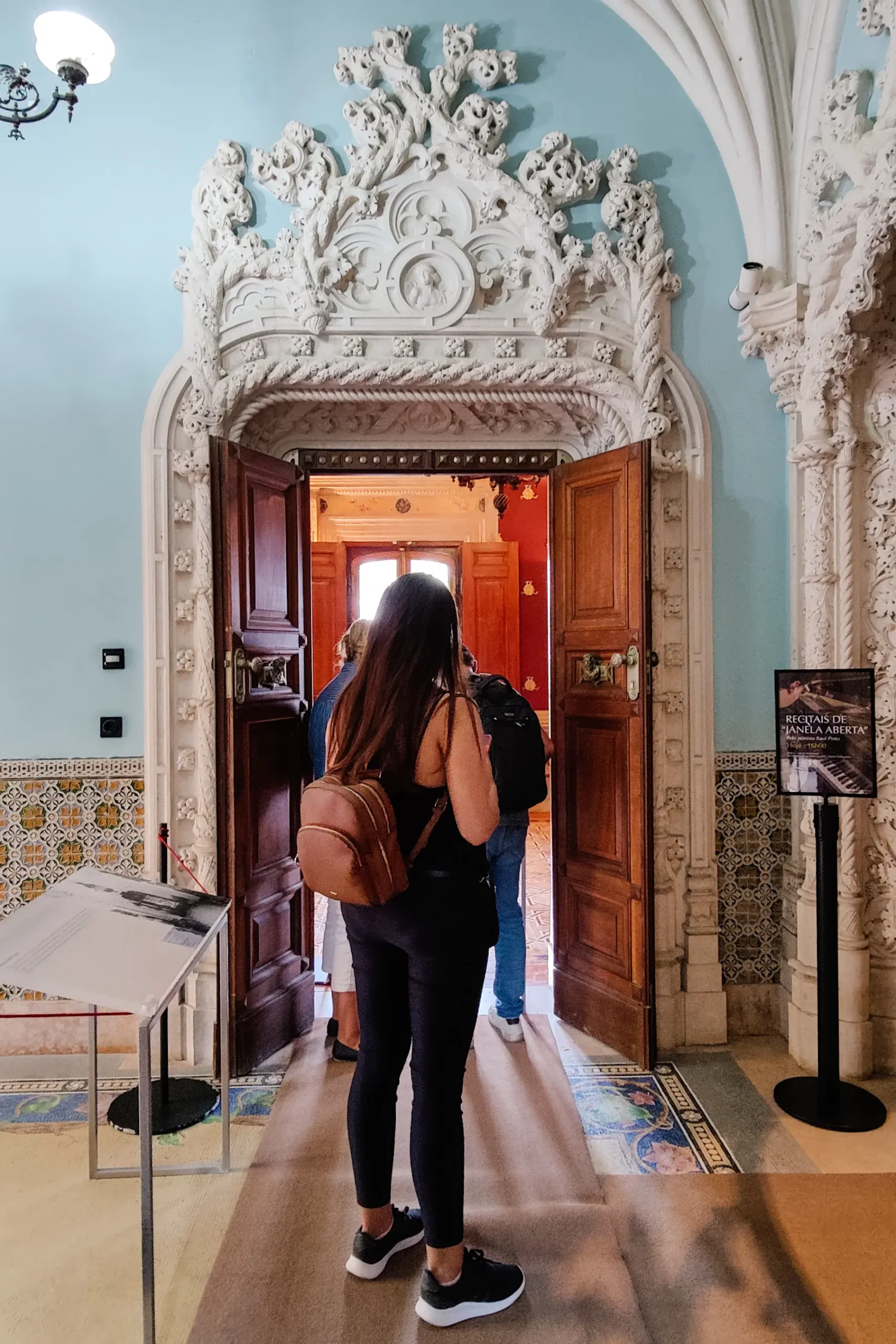 Woman wearing black walking towards an arch decorated with Gothic white plaster surrounded by a light blue wall inside Quinta da Regaleira.
