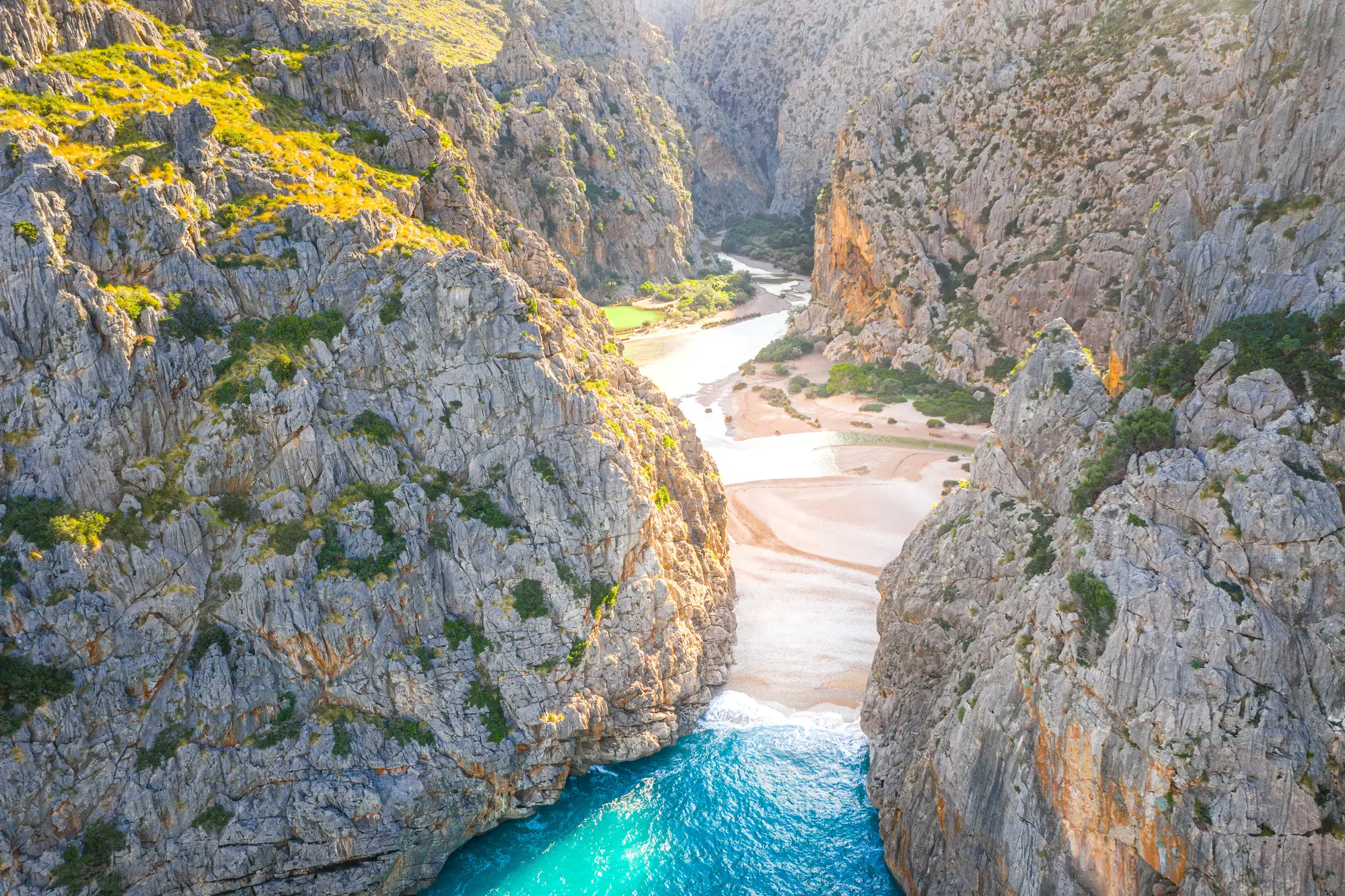 View from above of Torrente de Pareis in Mallorca, a large gorge with a pebbled beach and turquoise water.